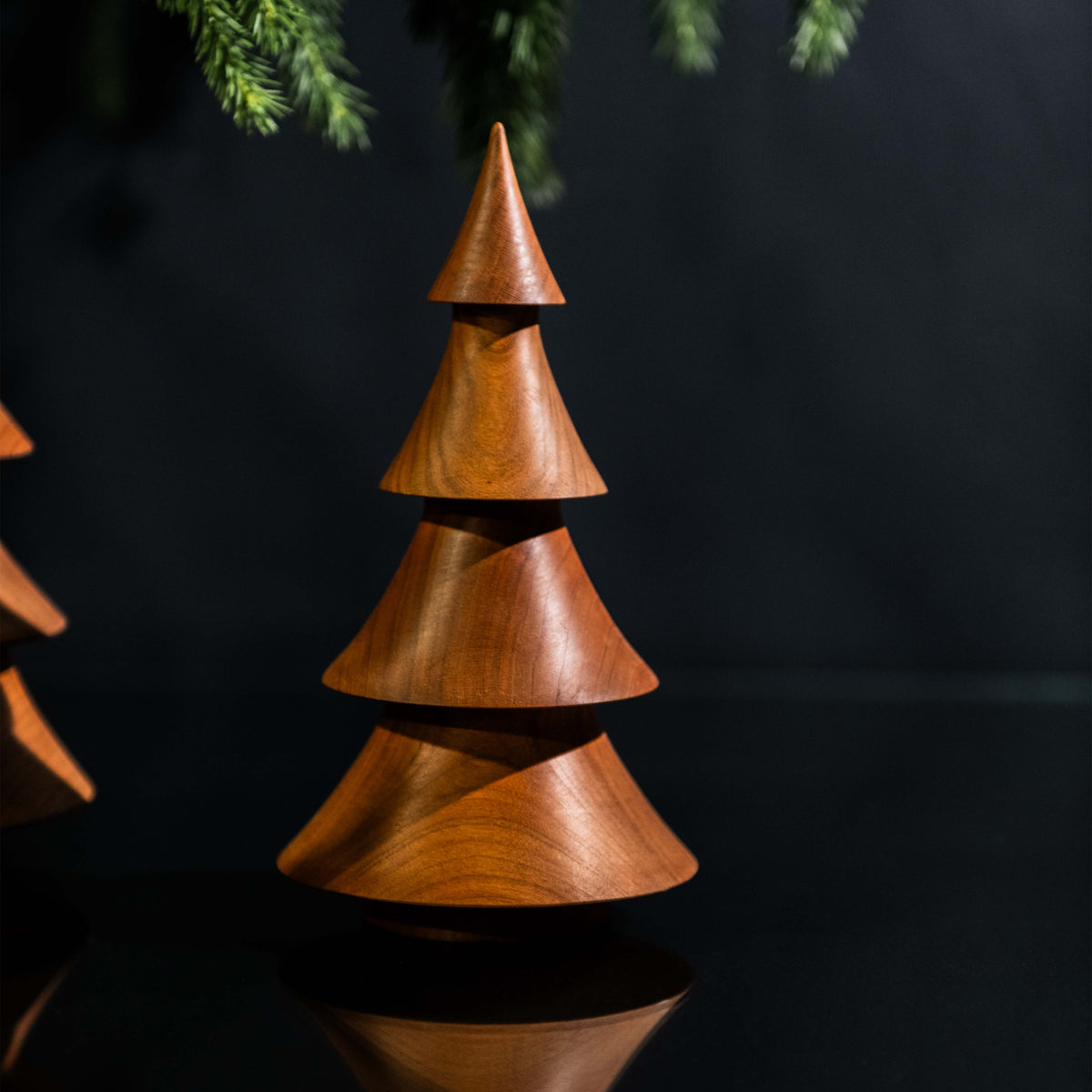 Stacked cherry wood cone pieces forming a tree shape with evergreen branches above on dark background.