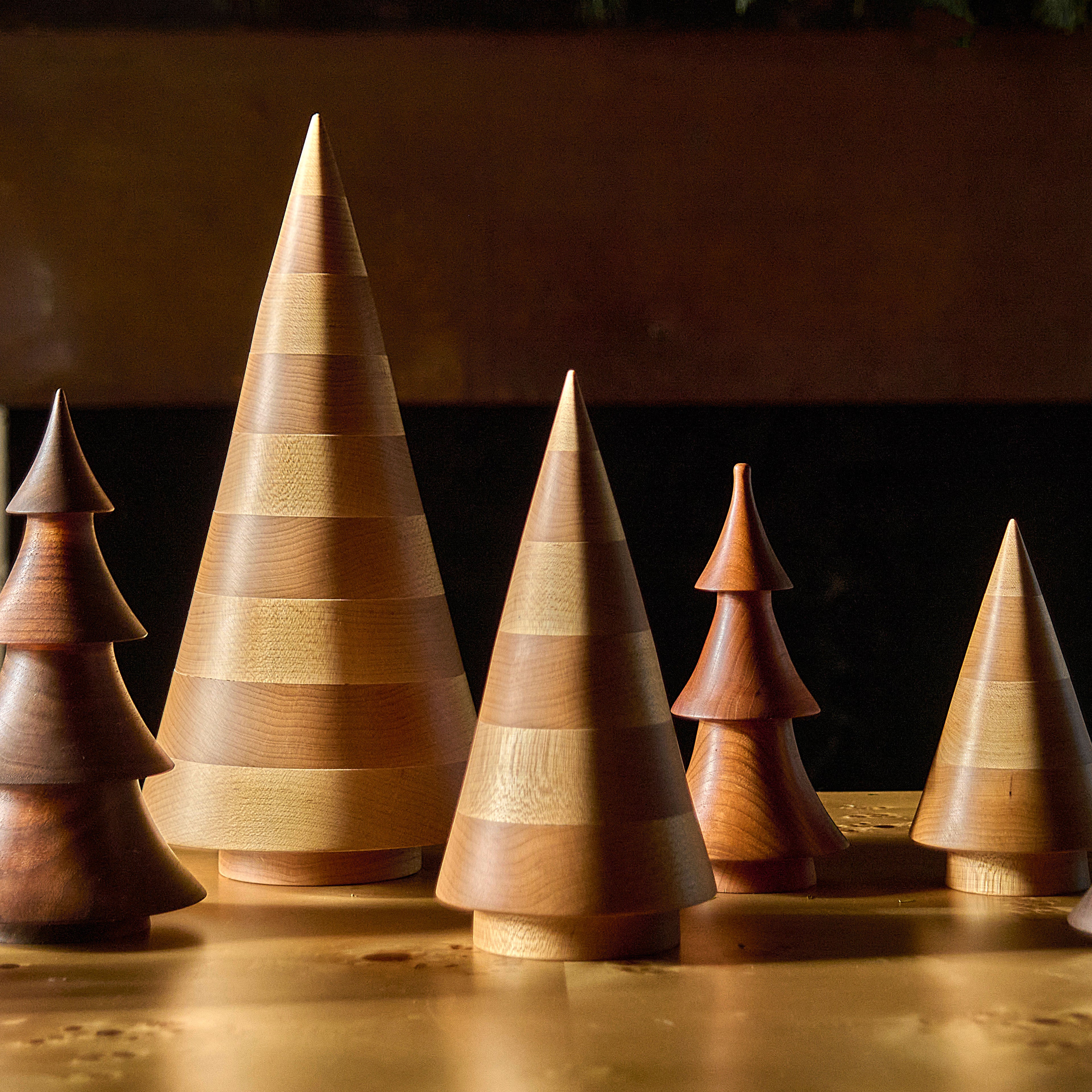 Five wooden cone-shaped evergreen trees in varying heights with horizontal bands, crafted from natural maple wood.