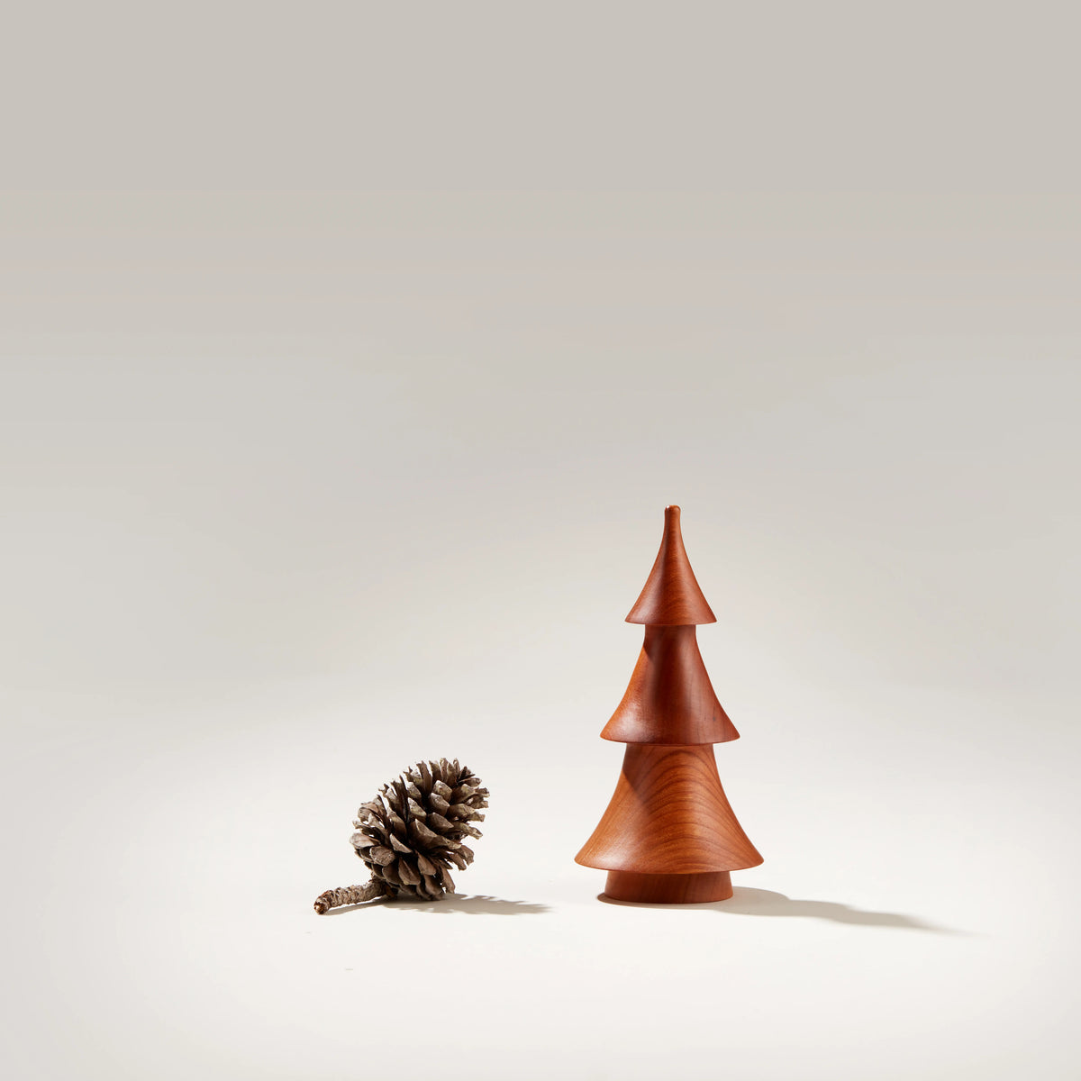 Cherry wood evergreen tree figurine with tiered cone shape next to a pine cone.