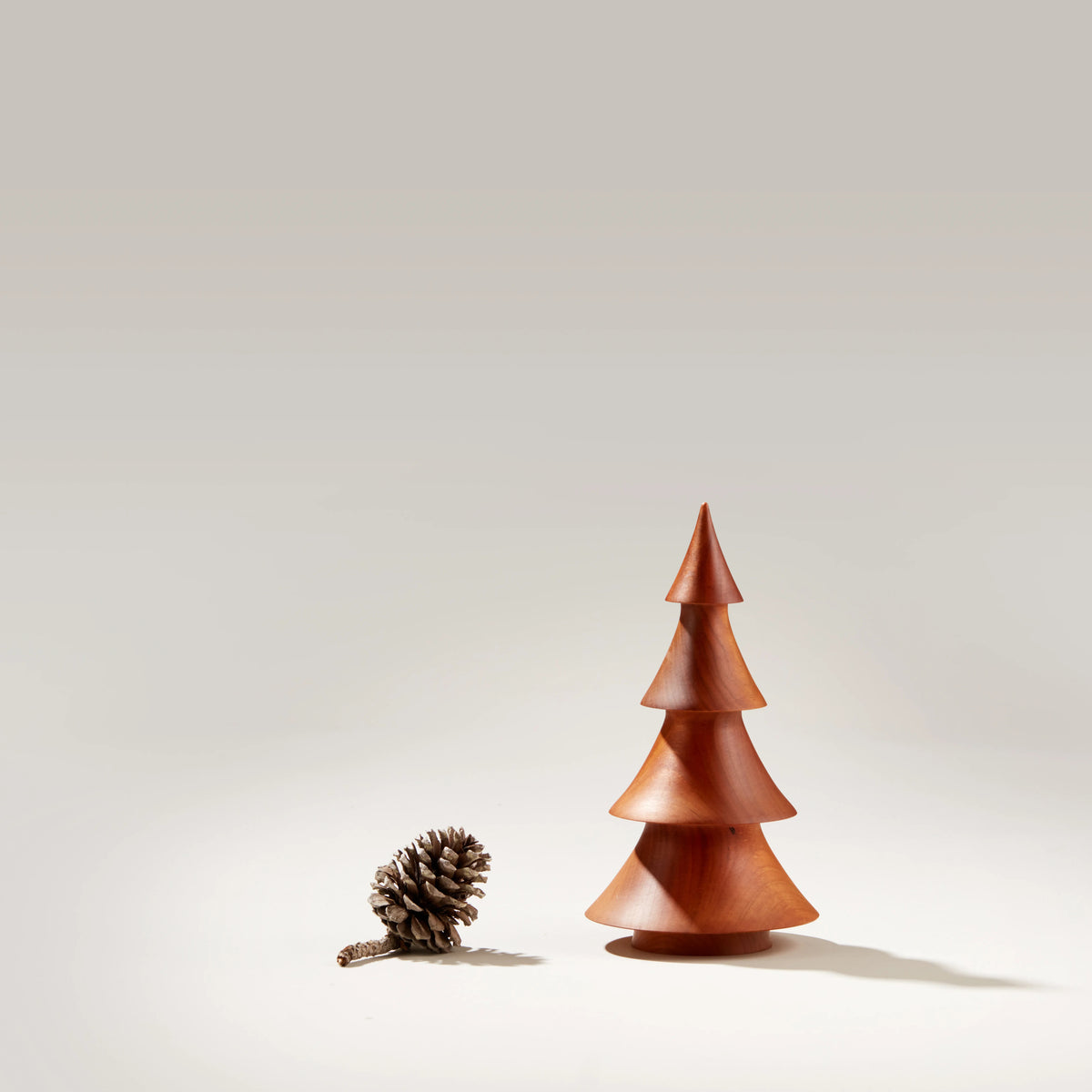 Wooden evergreen tree with four tiered cone sections in reddish-brown finish, displayed next to a pinecone.