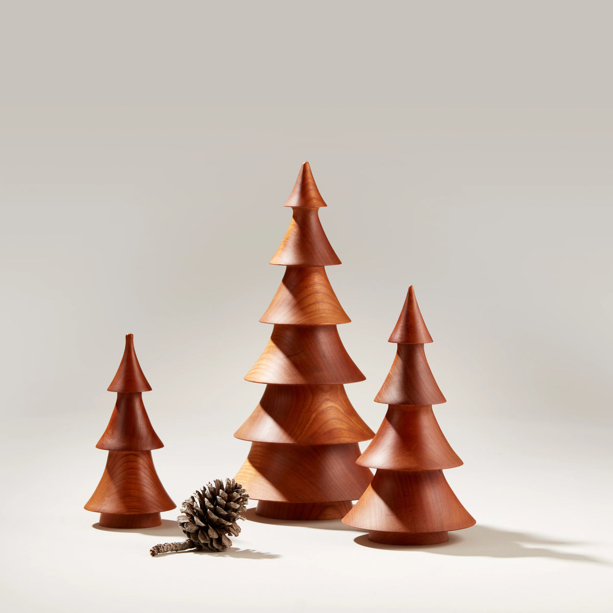 Three cherry wood evergreen tree decorations in graduated sizes with a pinecone.