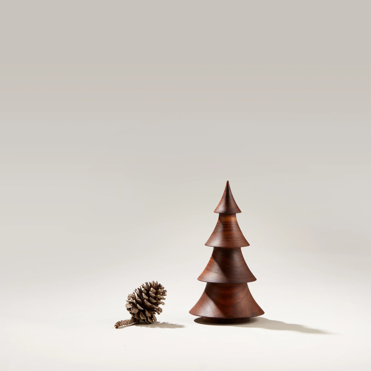 Walnut wood evergreen tree sculpture with tiered cone shape next to a pinecone.