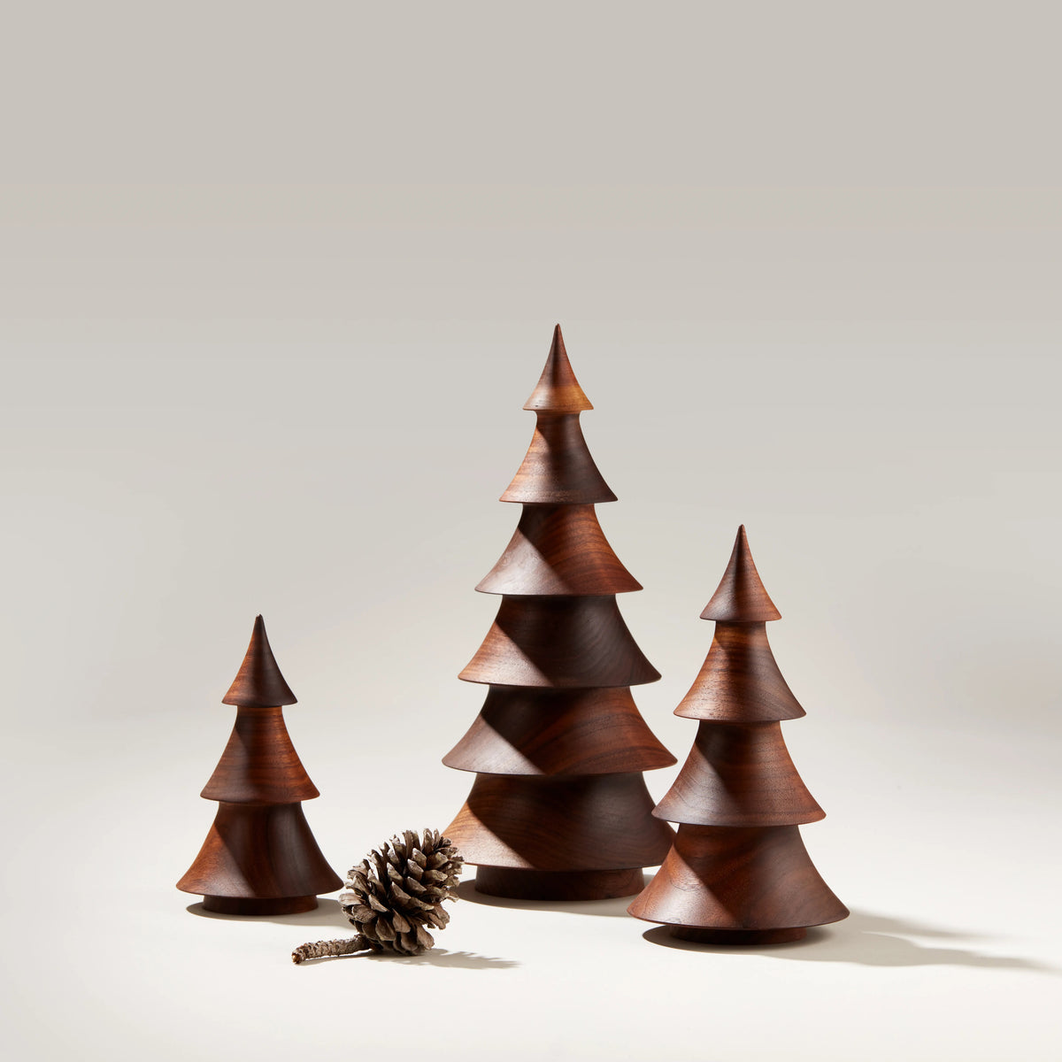 Three wooden evergreen tree decorations in dark walnut with a pinecone, arranged in graduating sizes.