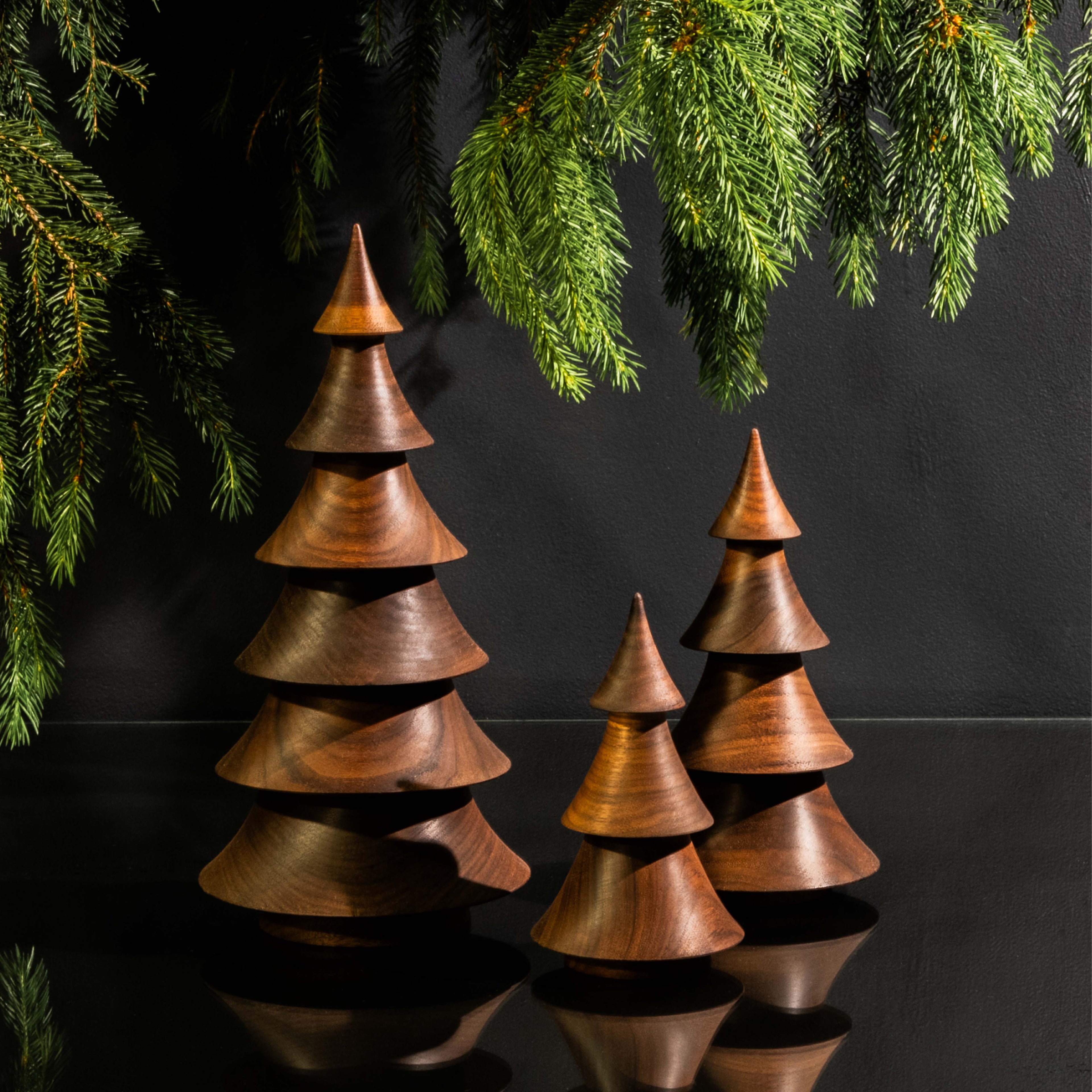 Three stacked walnut wood cone-shaped trees with varying heights and evergreen branches overhead.