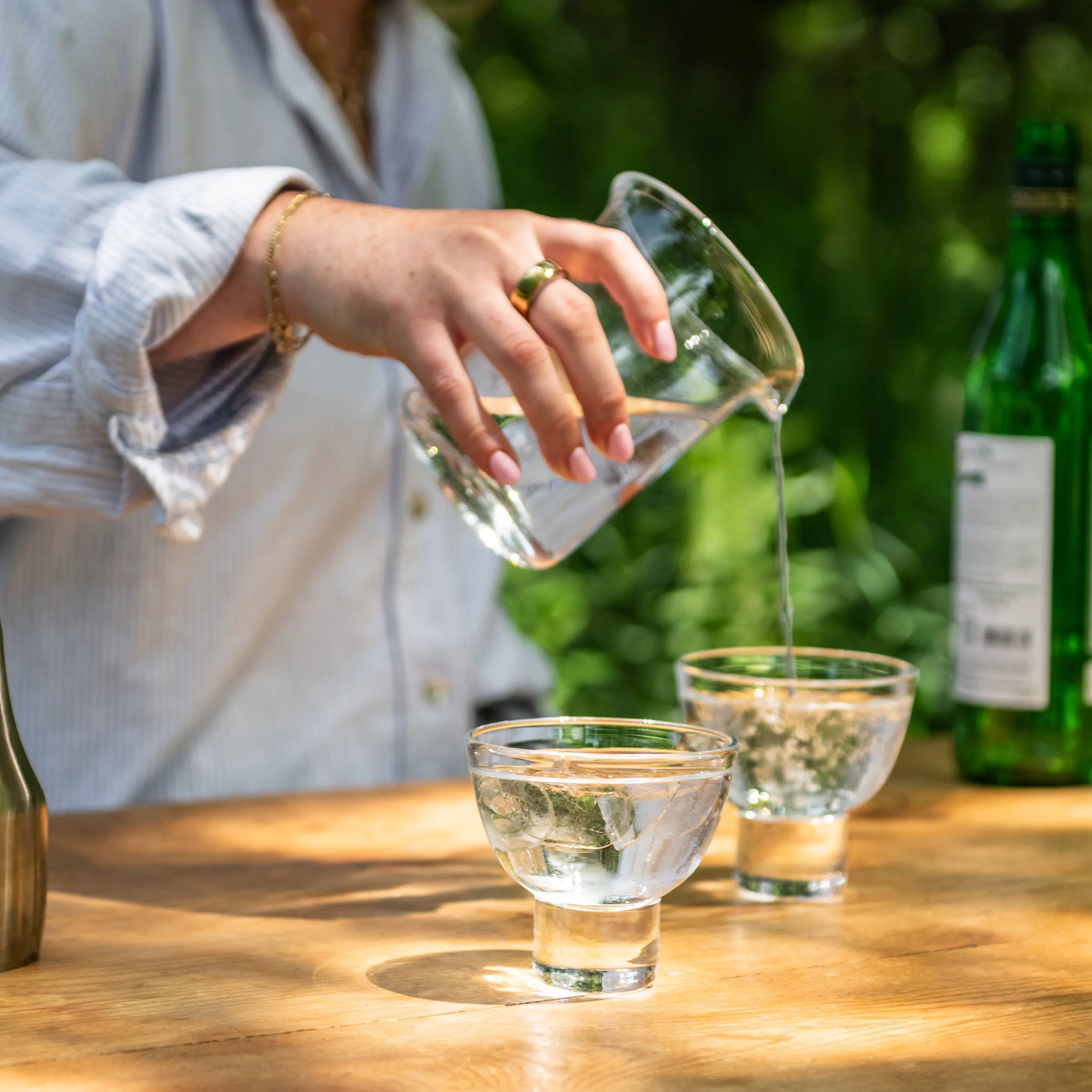 Clear glass pitcher with gold rim pouring liquid into matching glasses on wooden surface.