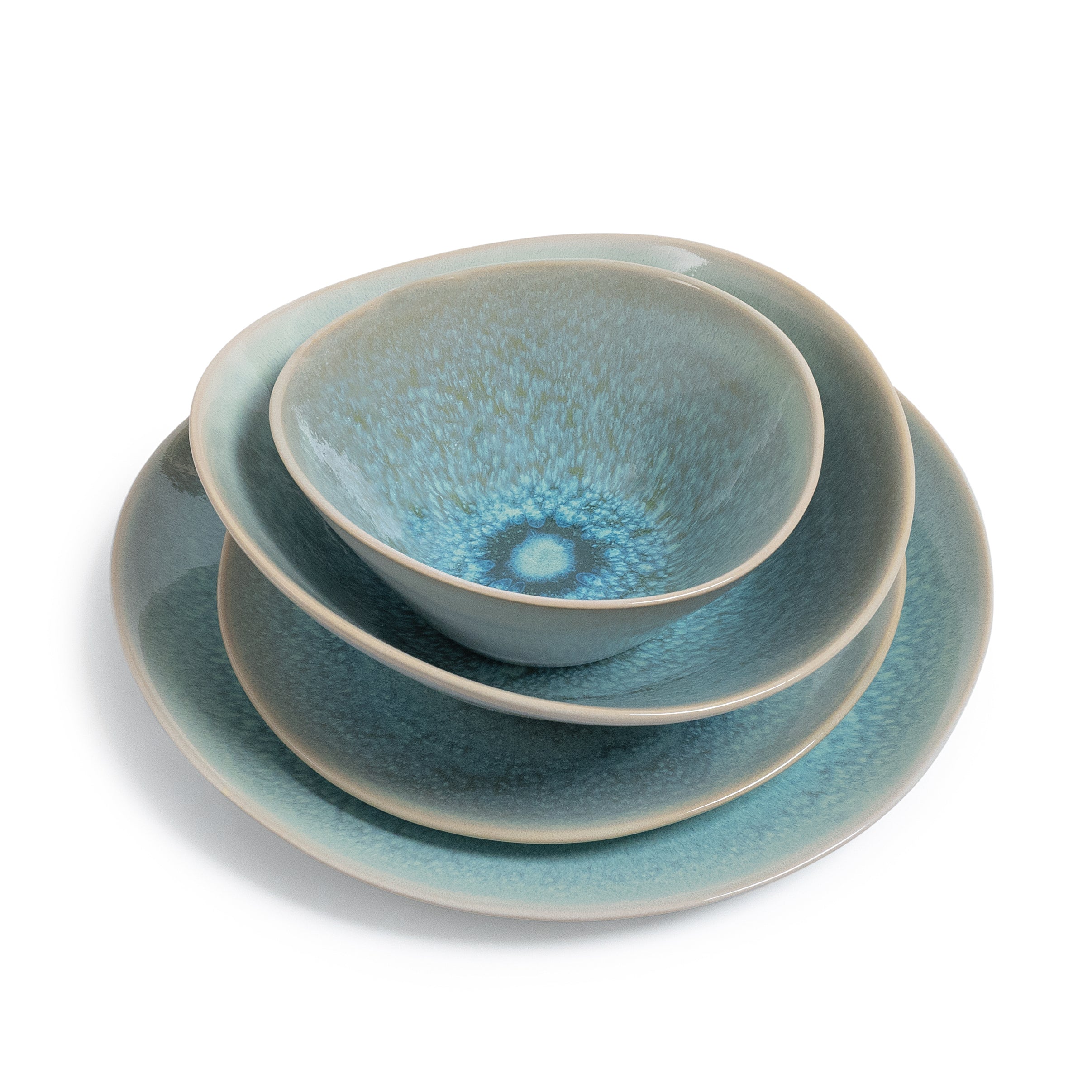 Stacked dinnerware set showing a blue-green glazed bowl, plate, and charger with textured finish and cream-colored rim.