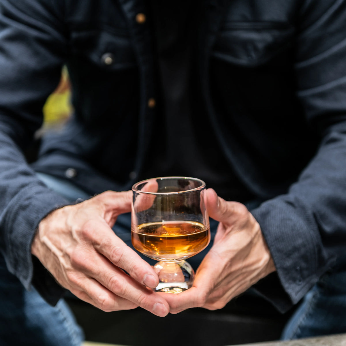 Person in dark jacket holding a glass of amber bourbon.