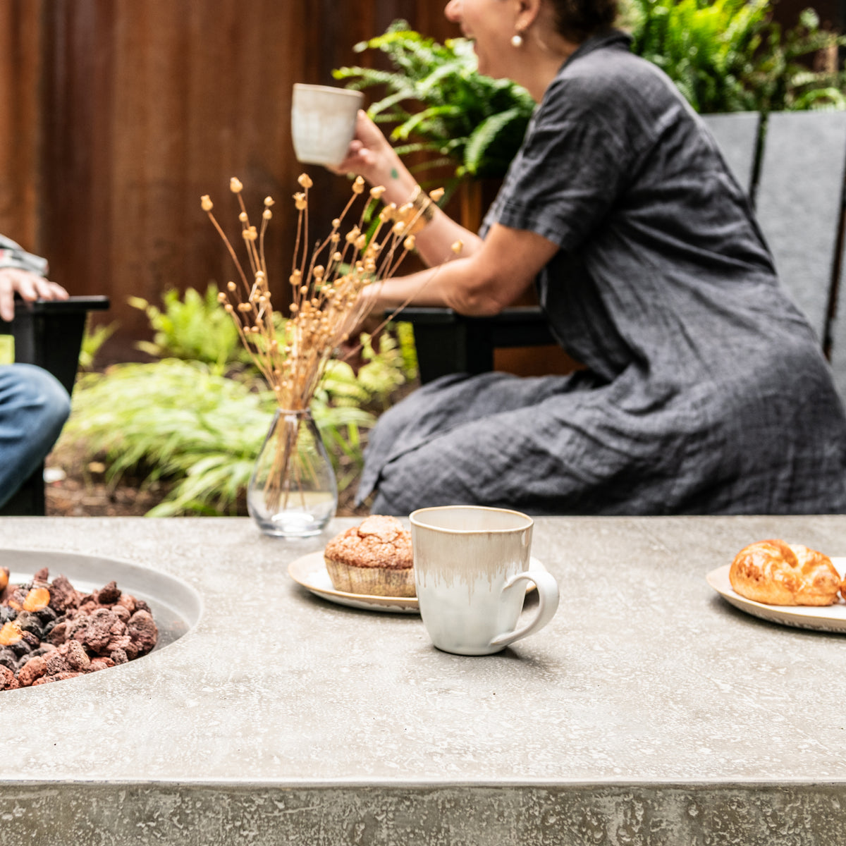 White ceramic mug with handle on table surrounded by plates of food and dried flowers.