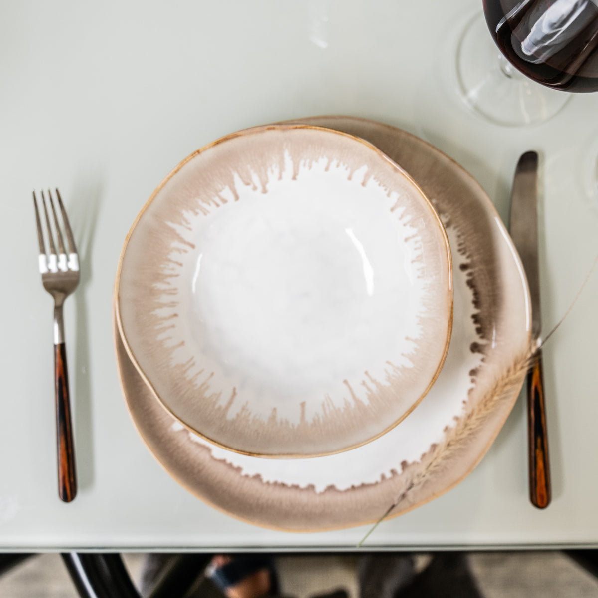 Two stacked plates with tan and white textured glaze, flanked by fork and knife on white surface.