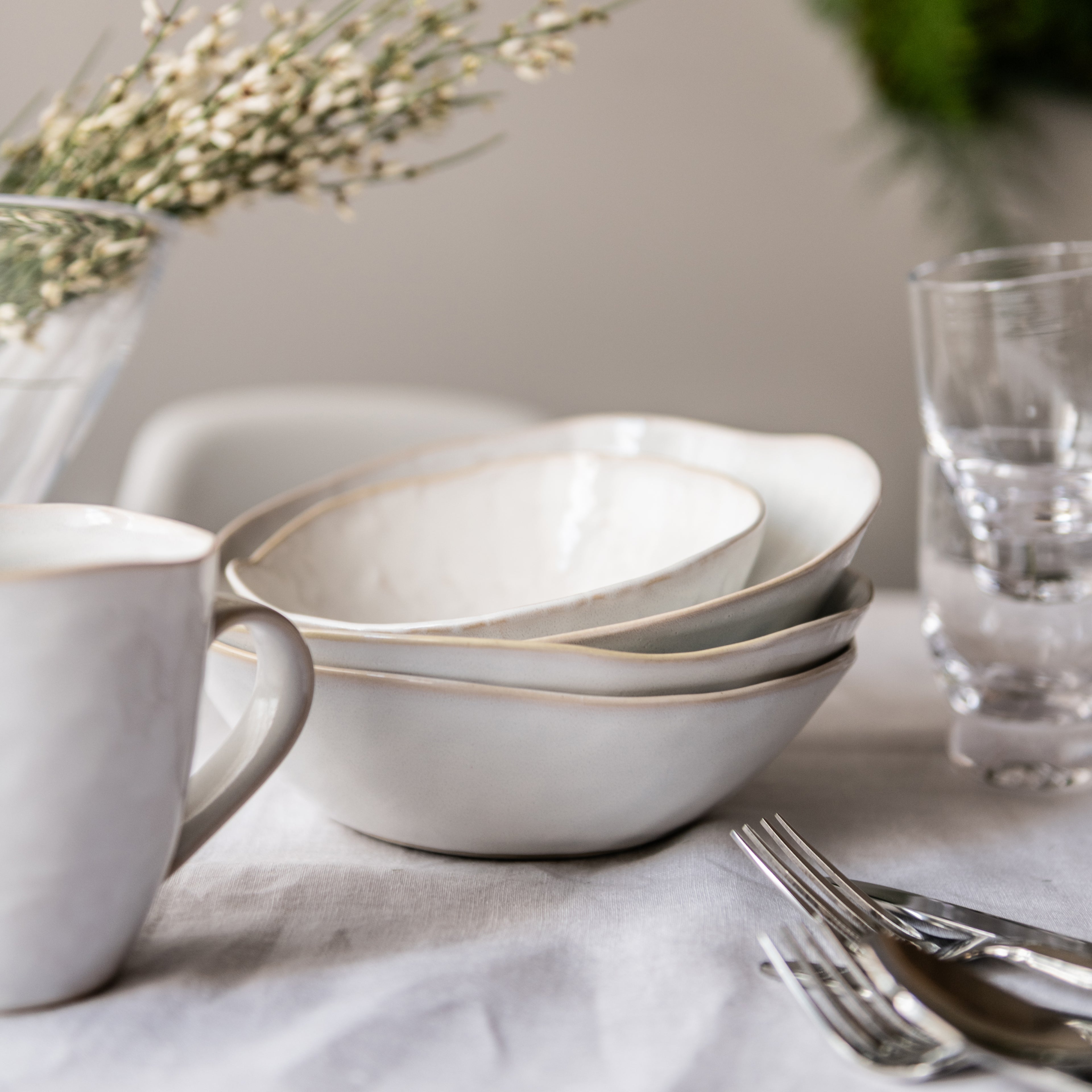 White dinnerware set with gold trim including stacked bowls, mug, and place setting on table.