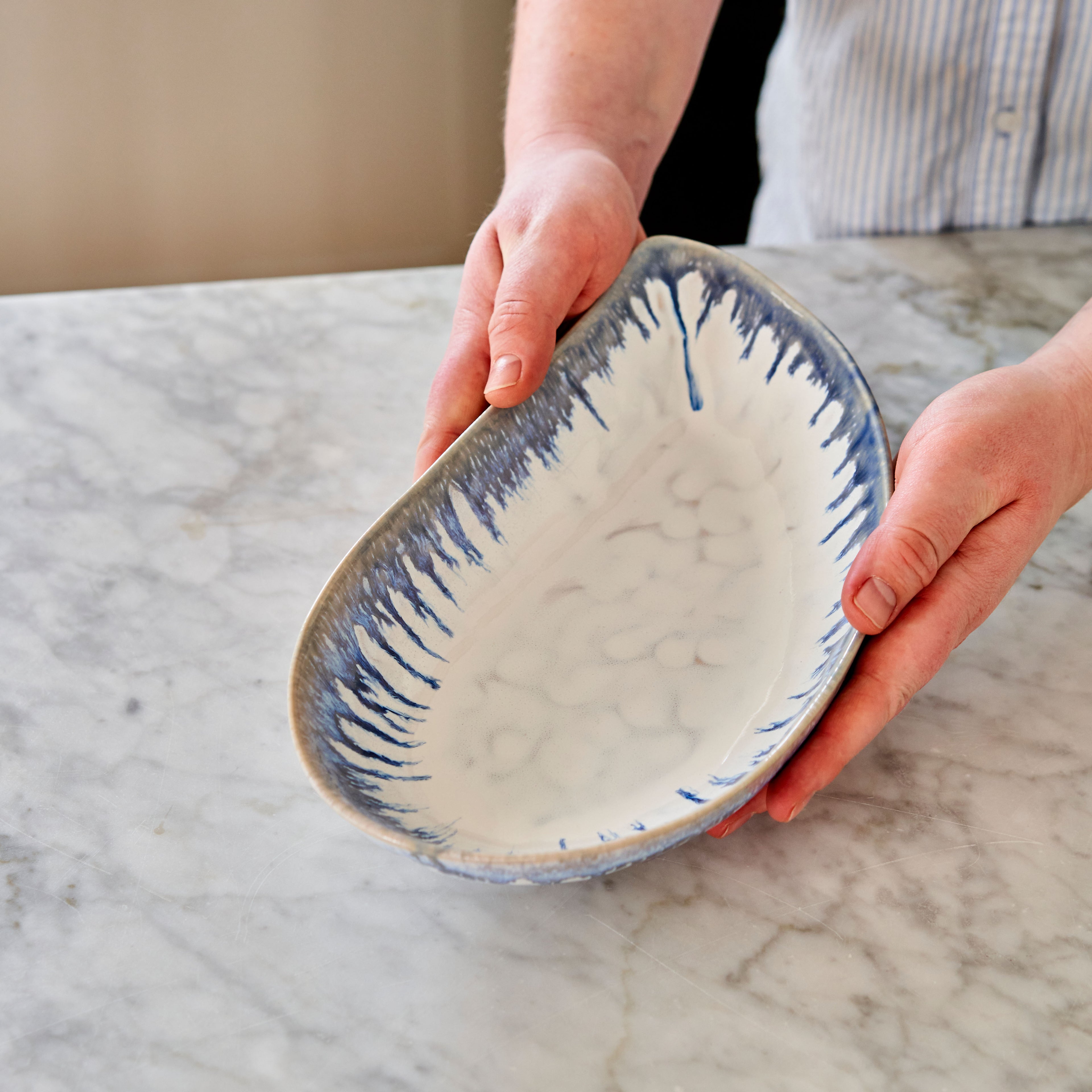 Cream and blue mussel shell-shaped ceramic bowl held in hands, showing interior with radiating blue lines.