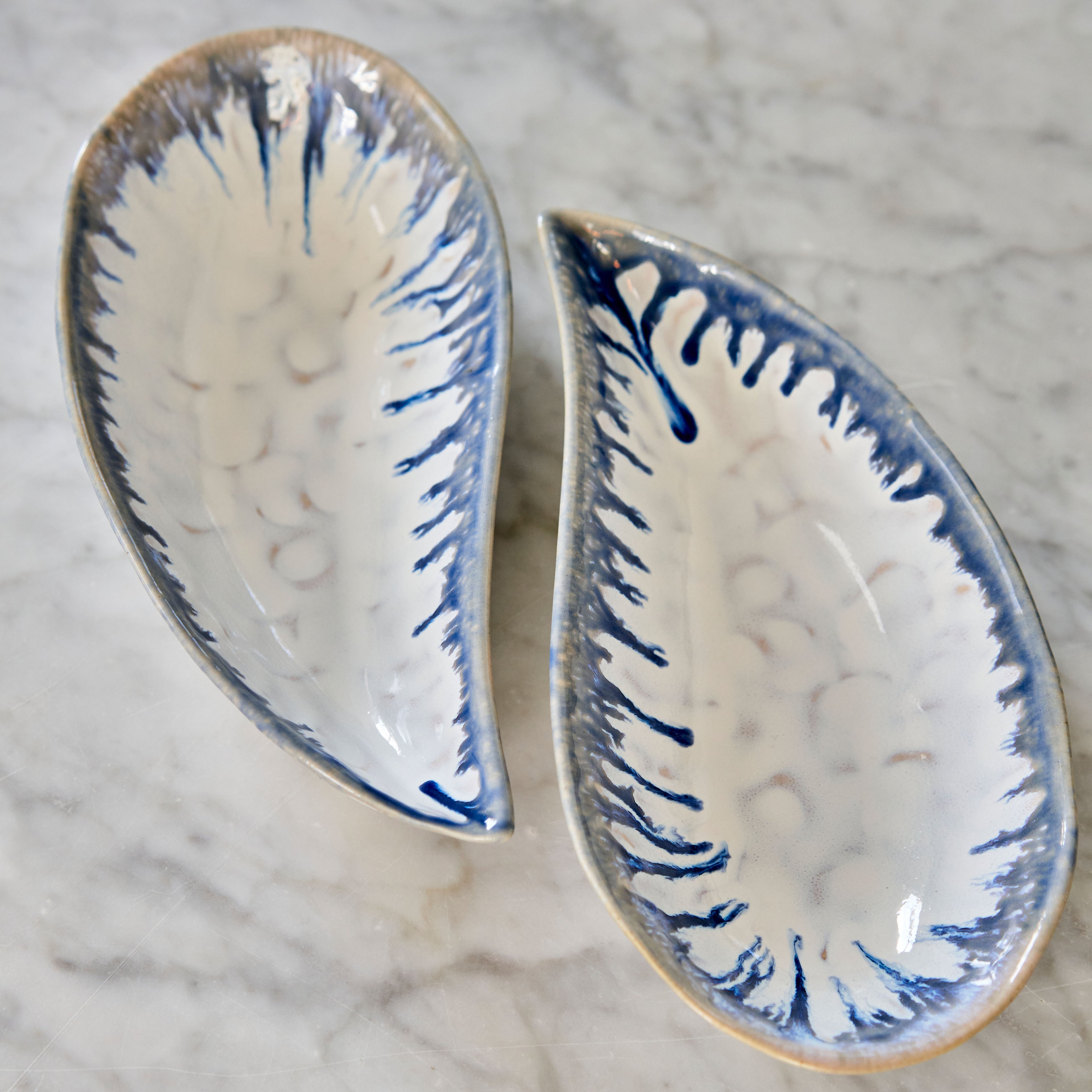 Two white ceramic mussel shell-shaped bowls with blue brush stroke detailing and tan rims.