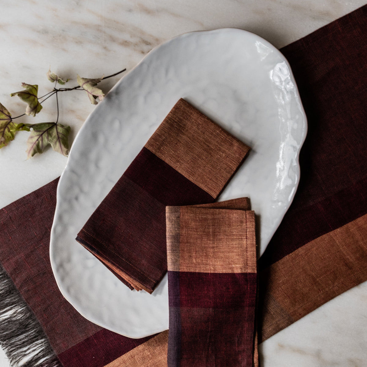 White oval platter with textured edge, displayed on marble surface with brown napkins and dried flowers.