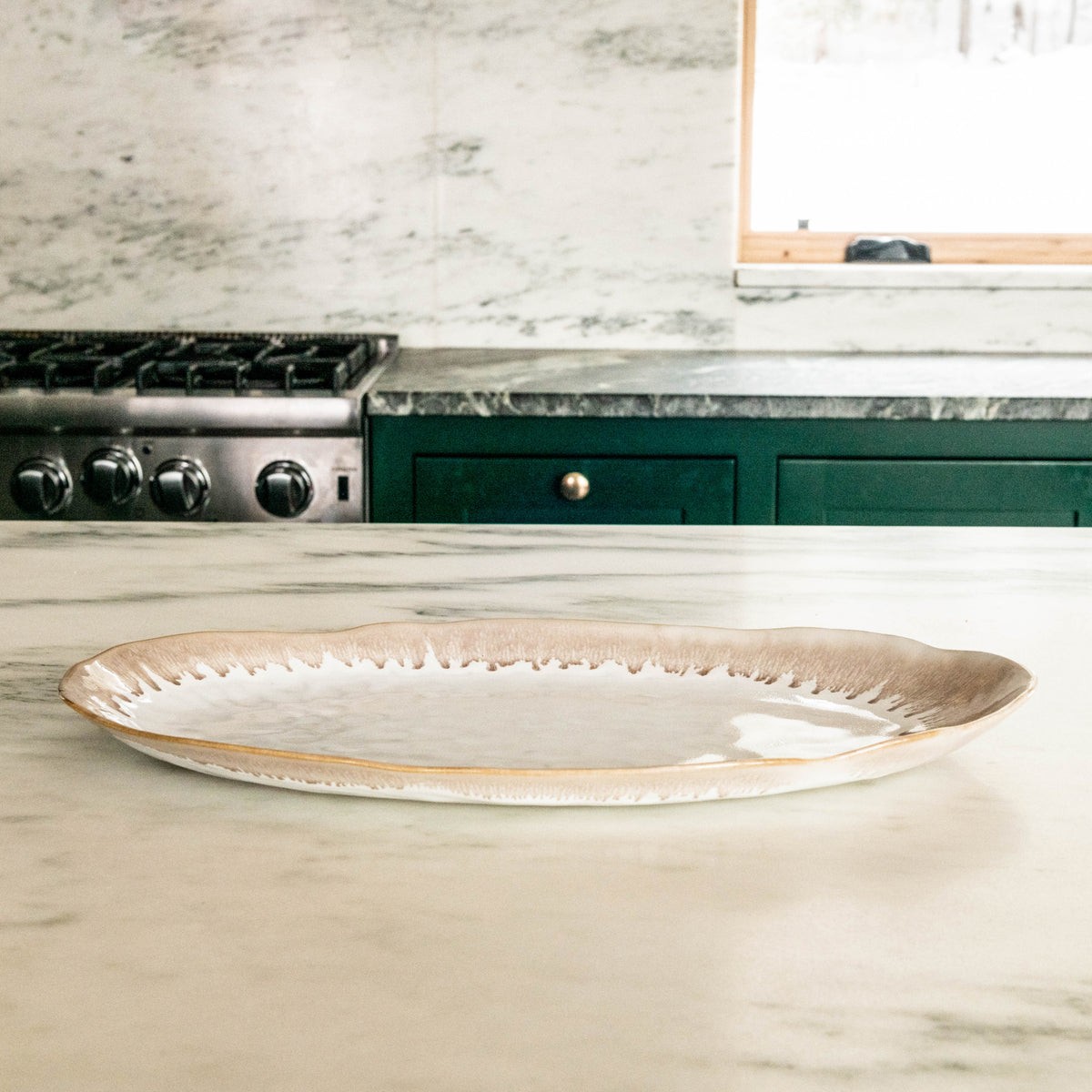 Oval ceramic platter with cream and tan glazed finish and textured rim, displayed on marble countertop.