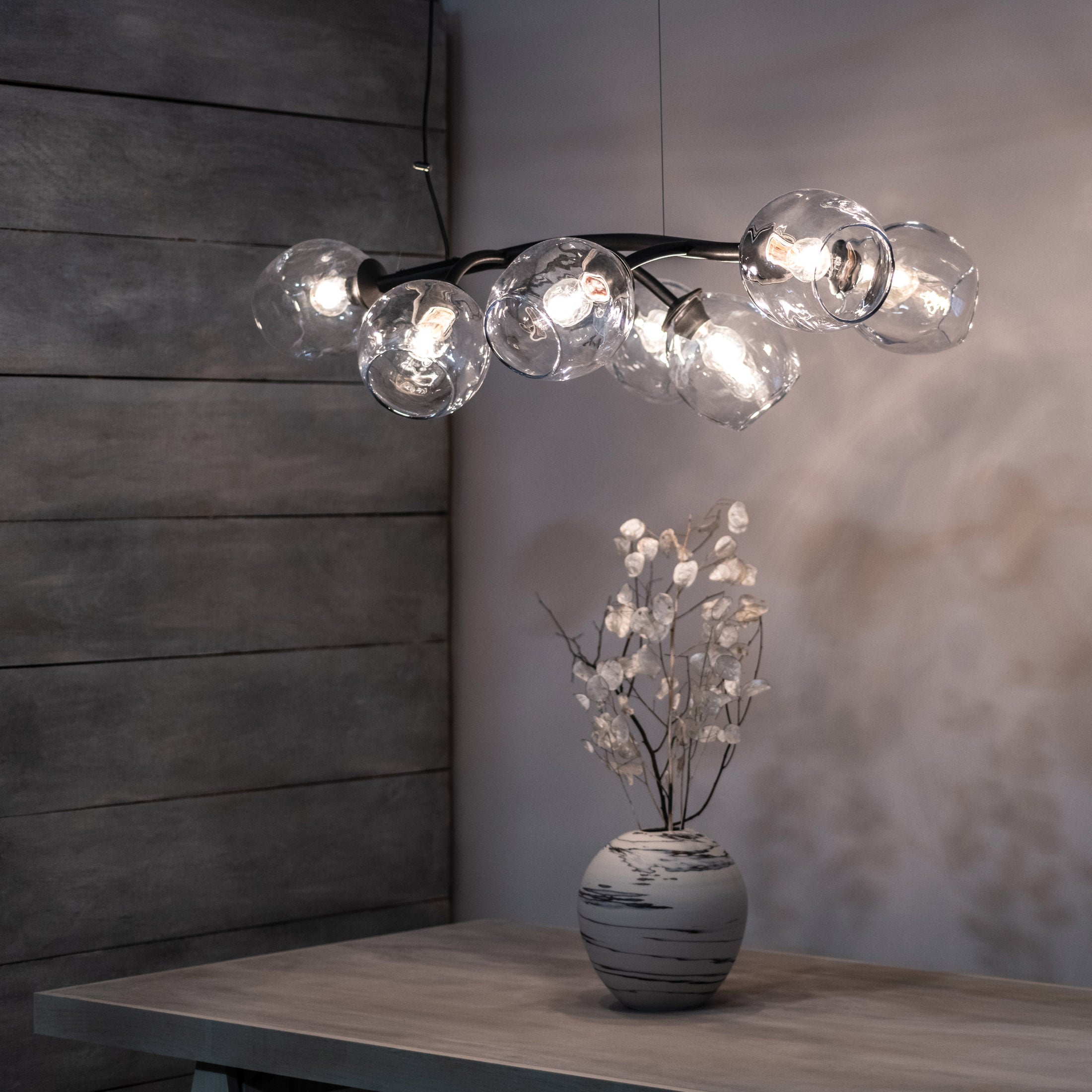 Black curved fixture with six clear glass globe pendants hanging at varying heights with illuminated bulbs inside.