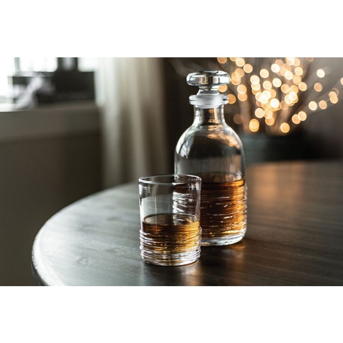 Glass decanter with stopper and matching whiskey glass filled with amber liquid on a marble table.