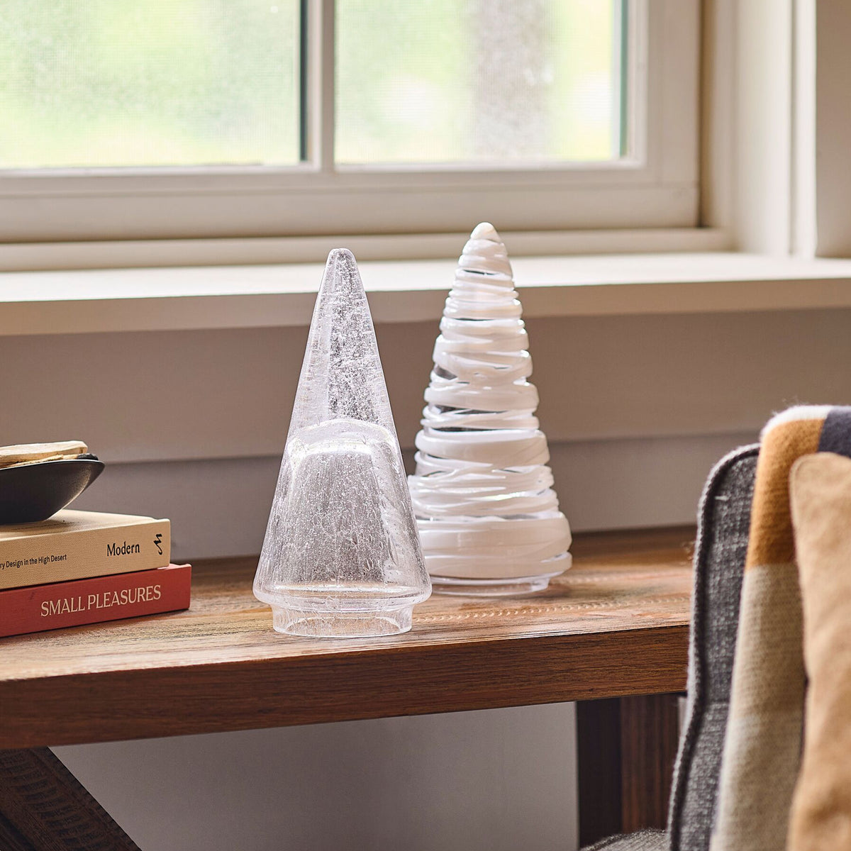 Two white conical decorative trees with textured finishes displayed on a wooden windowsill.