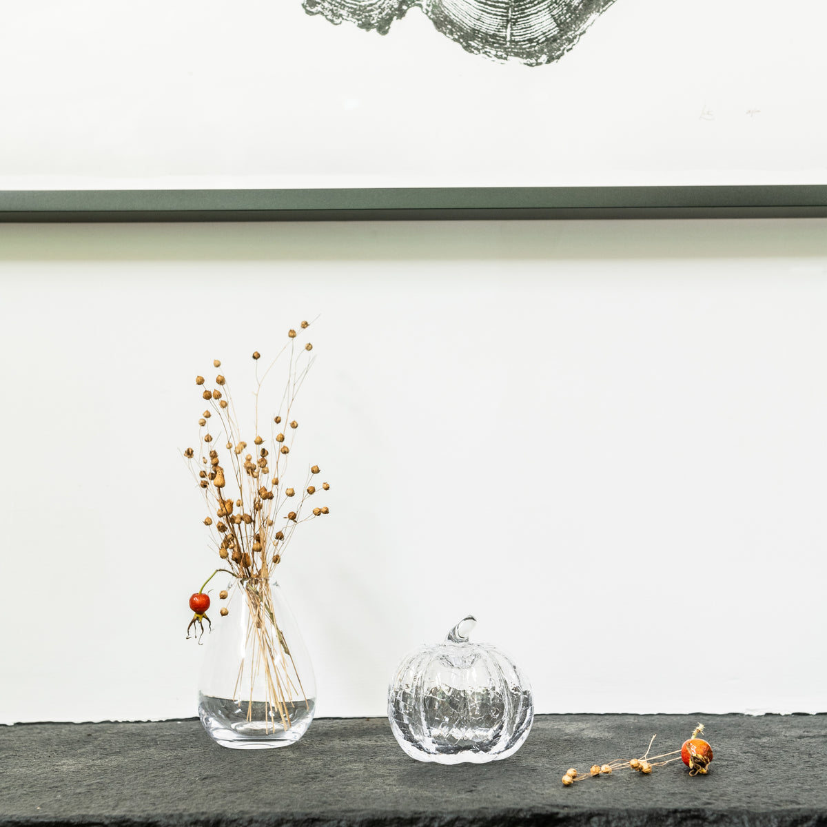 Clear glass pumpkin with crackle texture finish displayed next to dried botanicals in a vase.