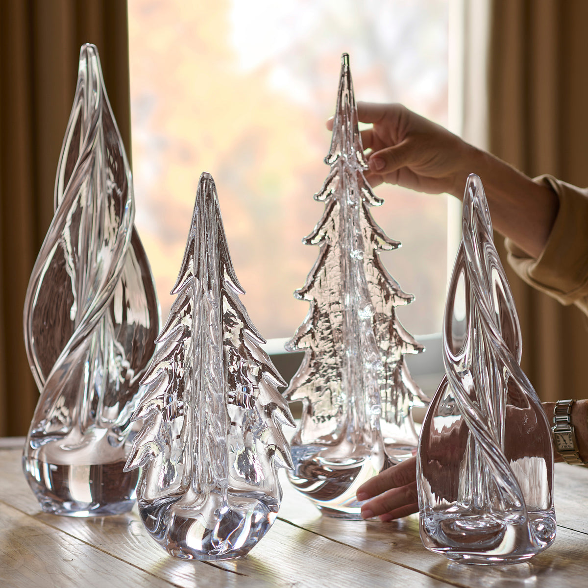 Four clear glass evergreen tree figurines with textured surfaces displayed on a wooden table.