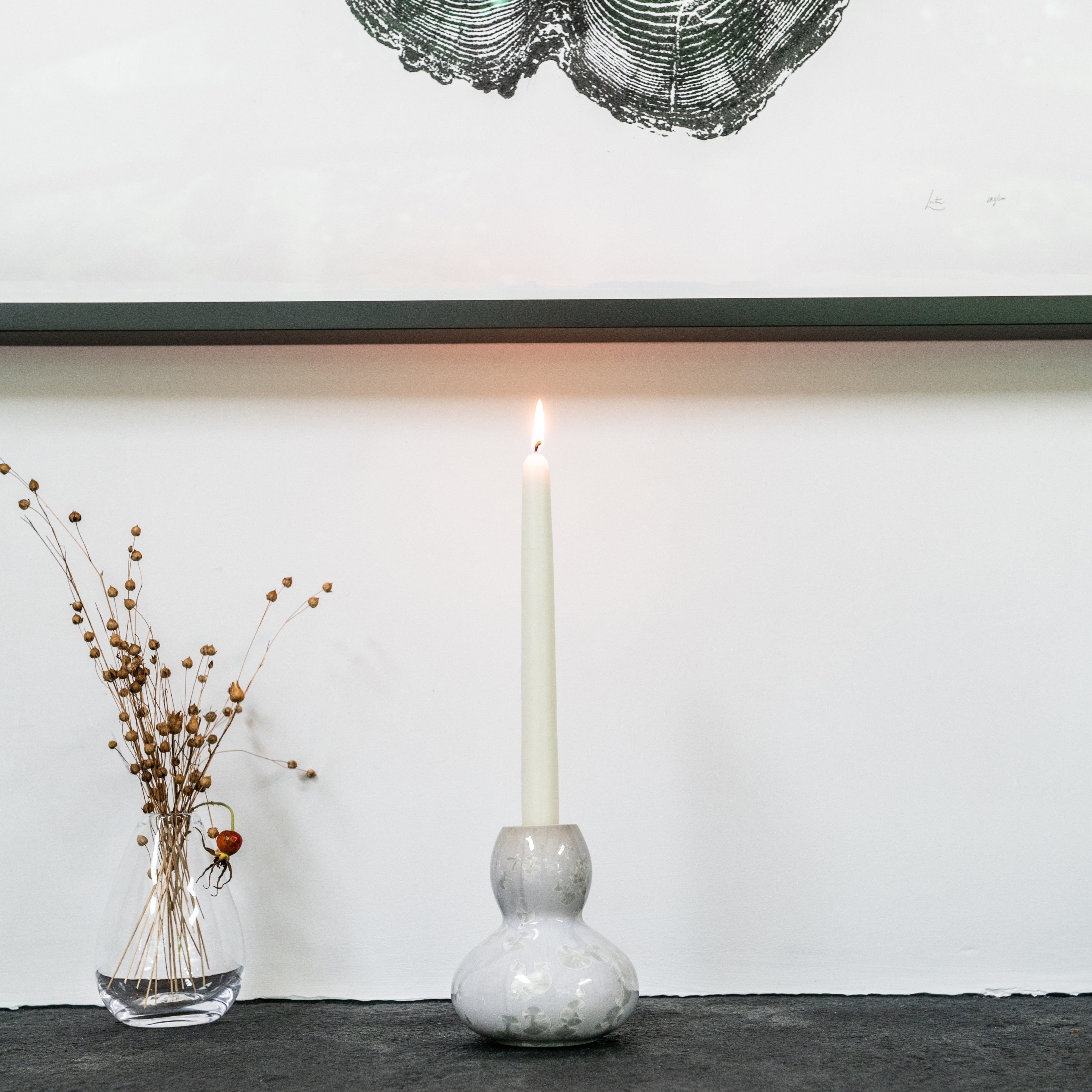 White ceramic candlestick with bulbous base holding a lit cream taper candle.