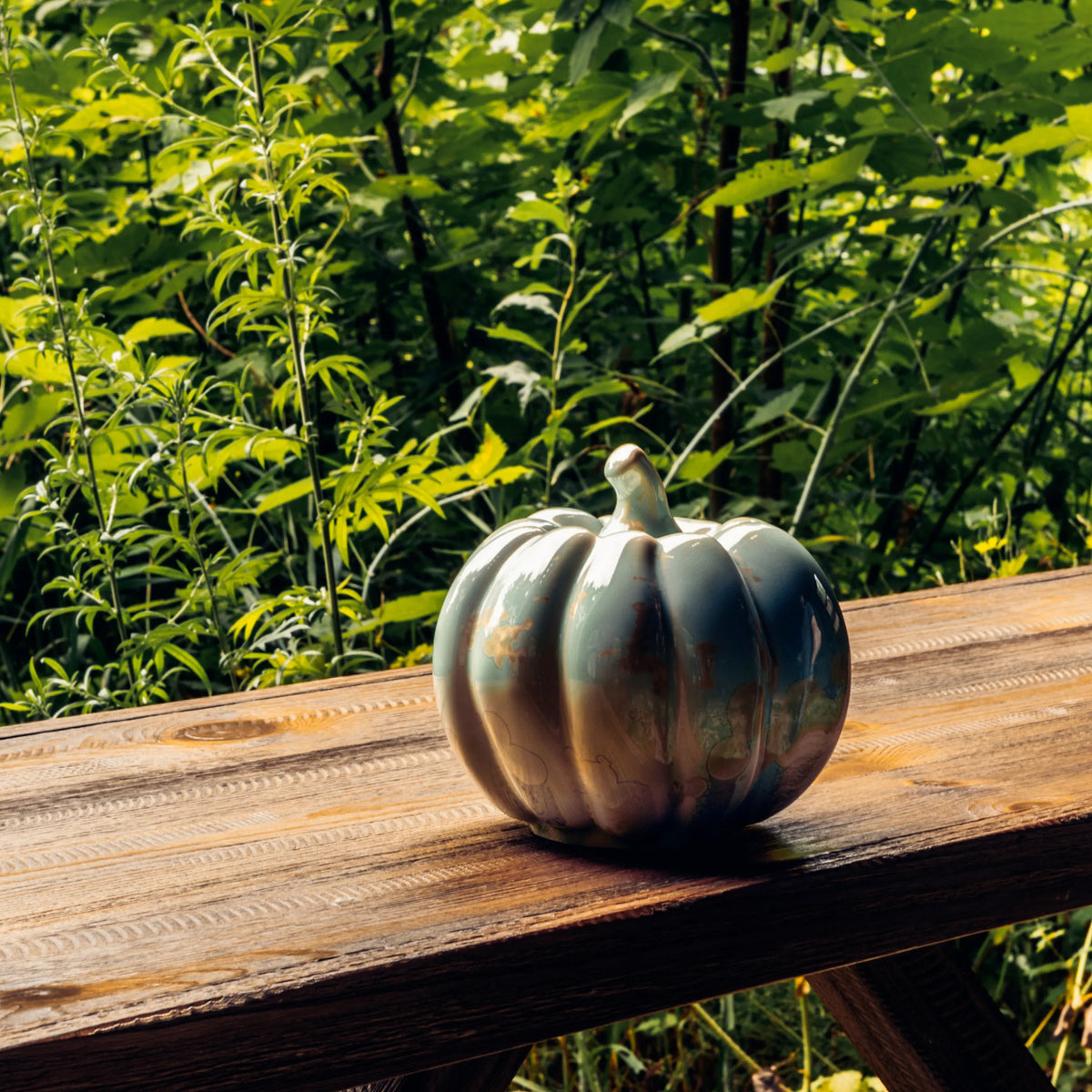 Metallic silver pumpkin-shaped decorative object on wooden surface with green foliage background.