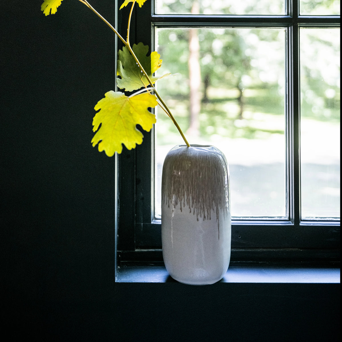 Bluff-colored ceramic vase with textured glaze pattern, holding yellow flower stems on windowsill.
