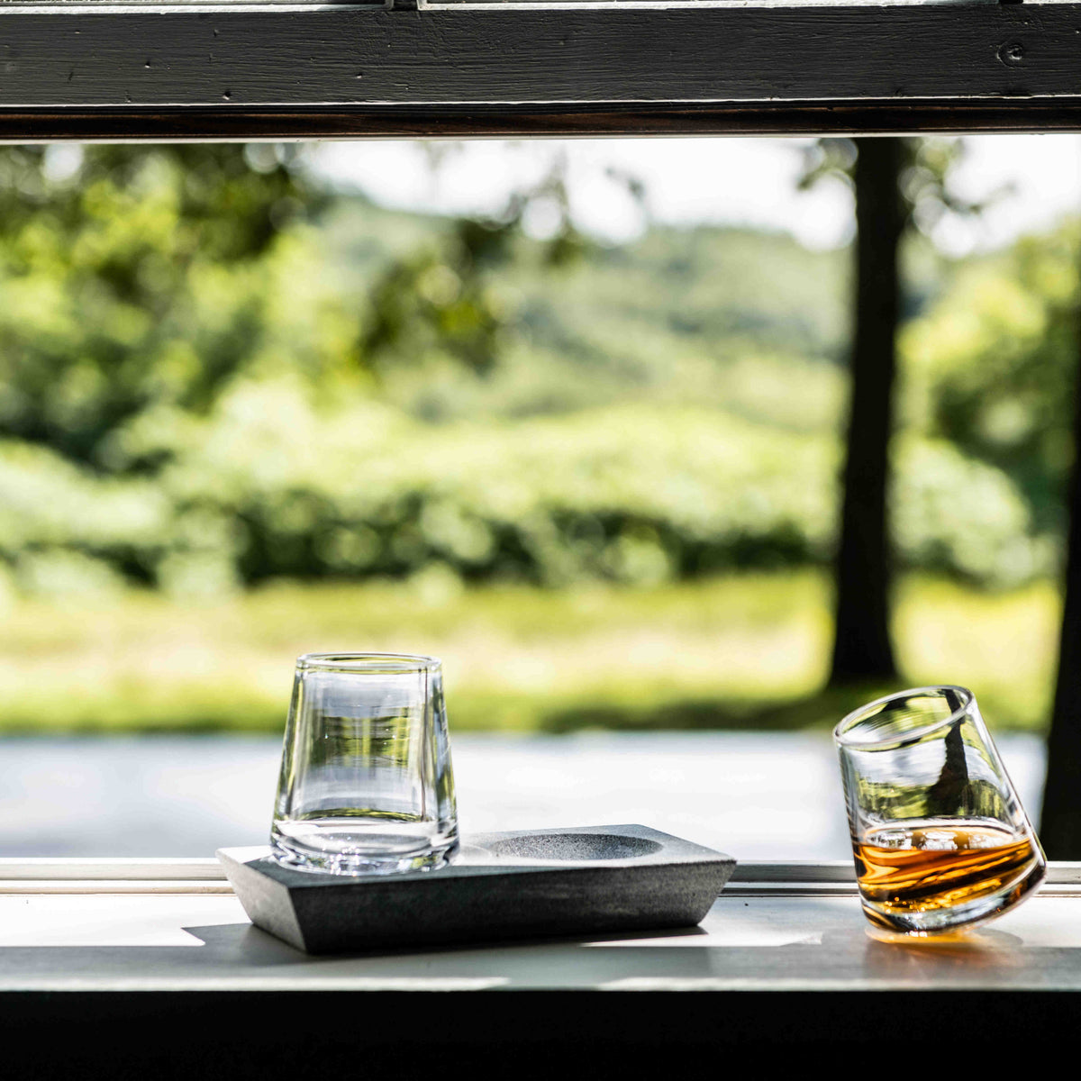 Two whiskey glasses with angled soapstone base holding one empty and one amber-filled glass.