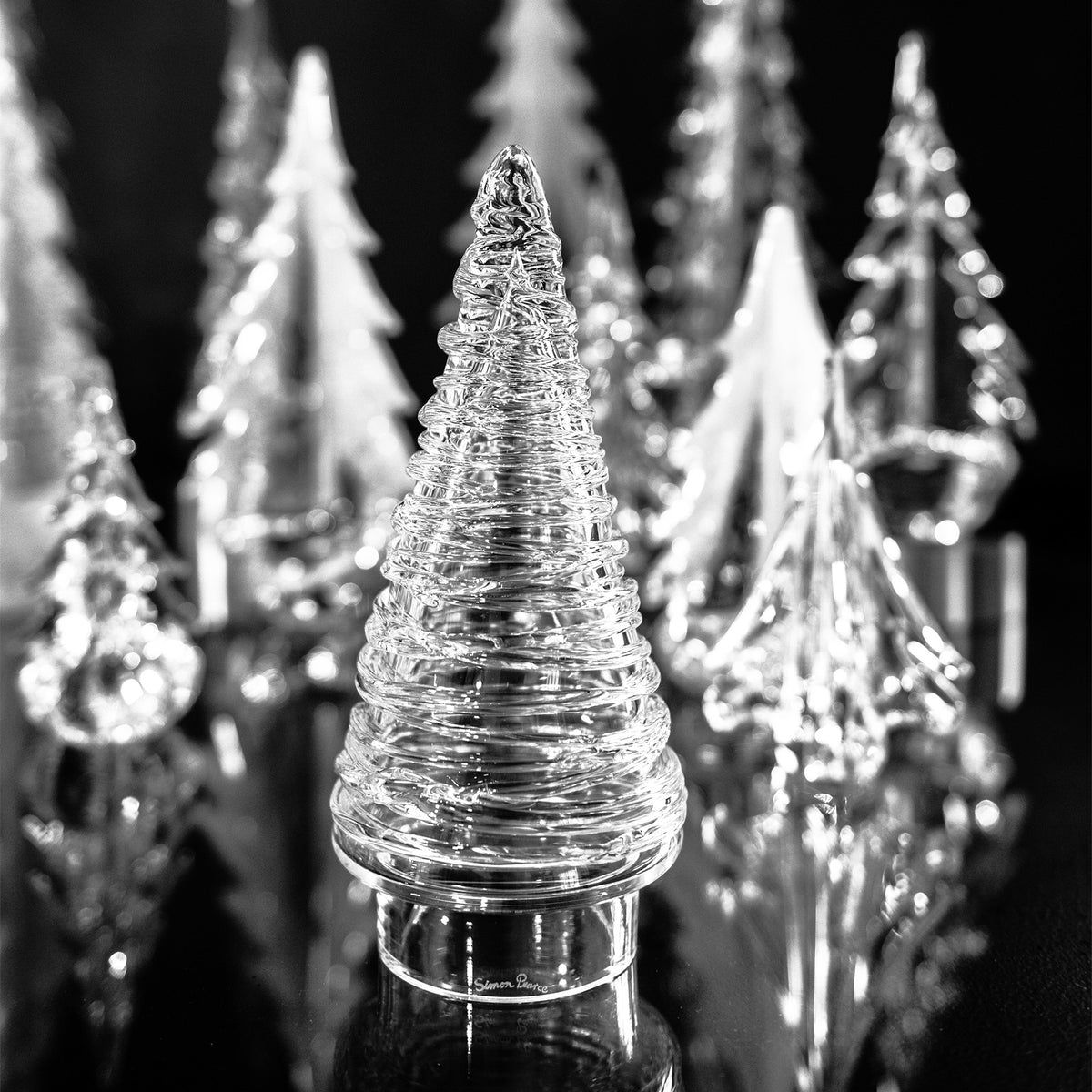 Clear glass cone-shaped tree with horizontal ridged pattern, displayed among blurred similar trees against black background.