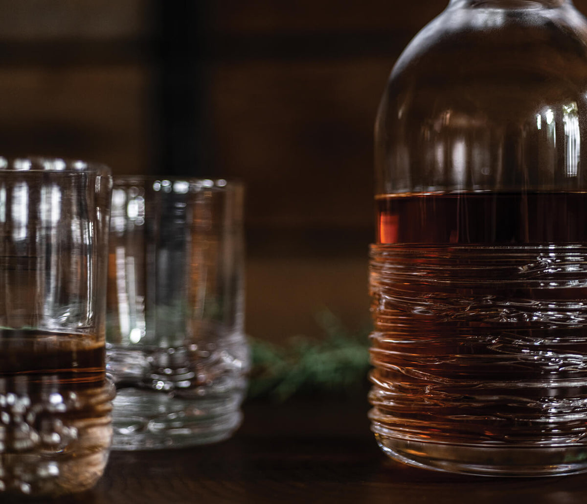 Whiskey bottle and two glasses filled with amber liquid on dark surface.