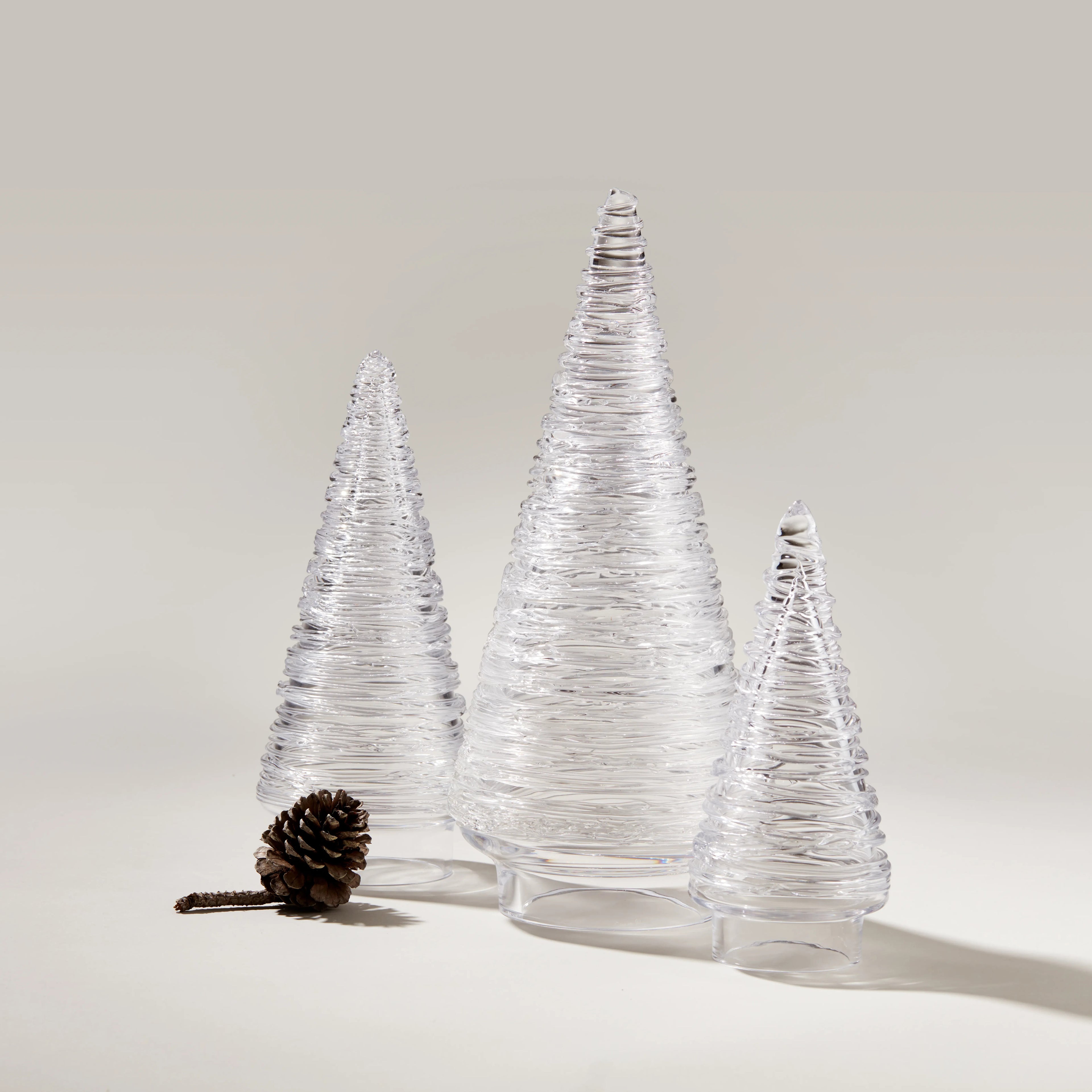 Set of three clear glass cone-shaped decorative trees with textured surfaces and a pinecone accent.