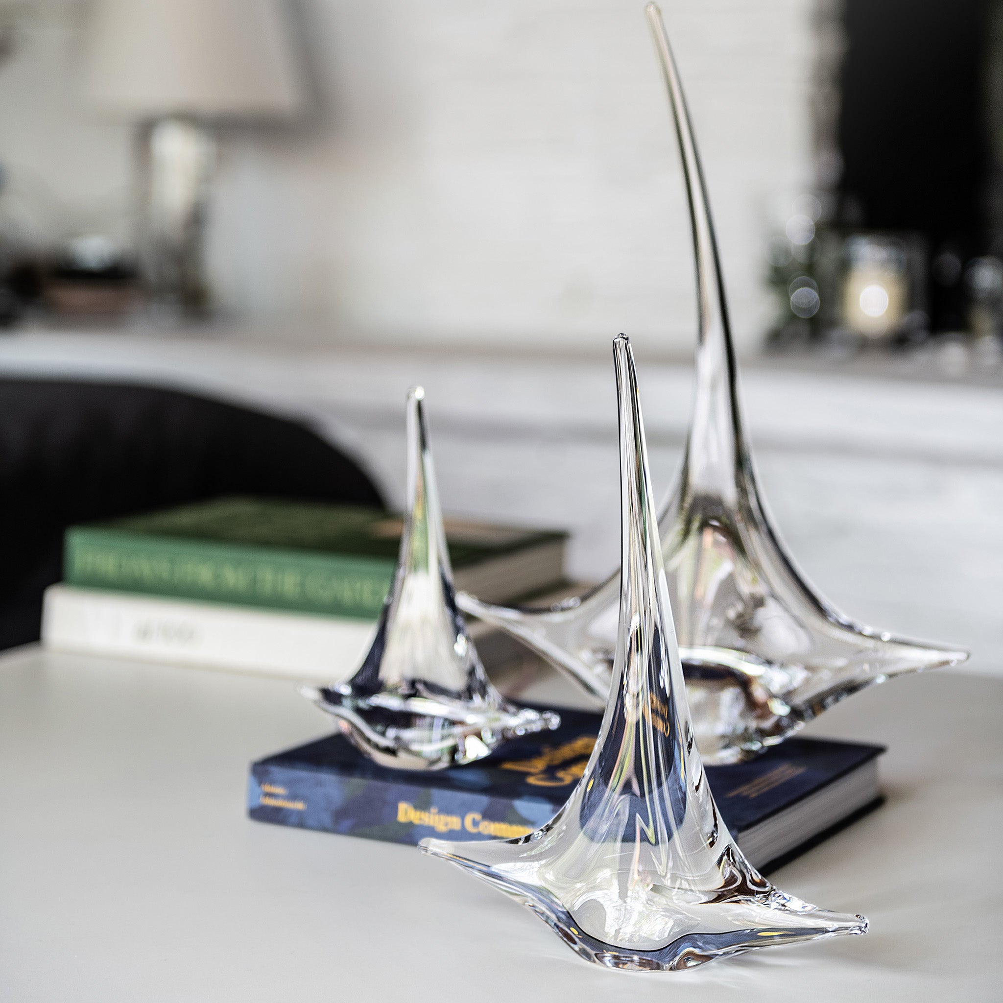 Clear glass sailboat figurines with pointed masts on dark bases, displayed on a desk.