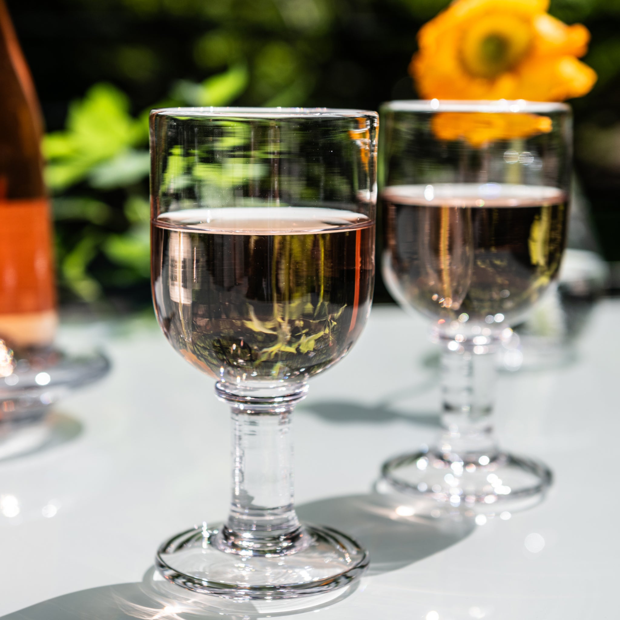 Two wine glasses filled with white wine on outdoor table with garden background.