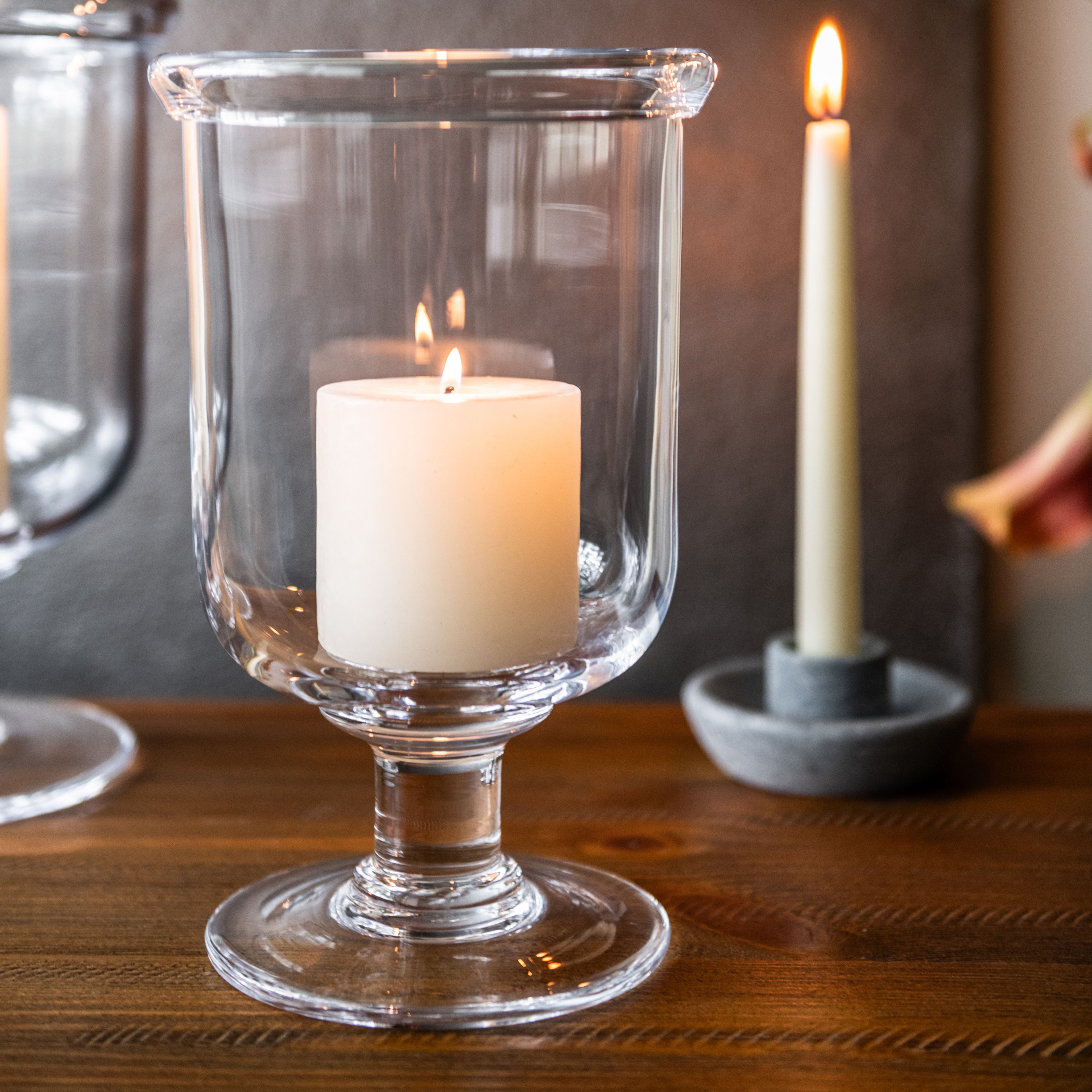 Clear glass hurricane candle holder with pedestal base containing white pillar candle.