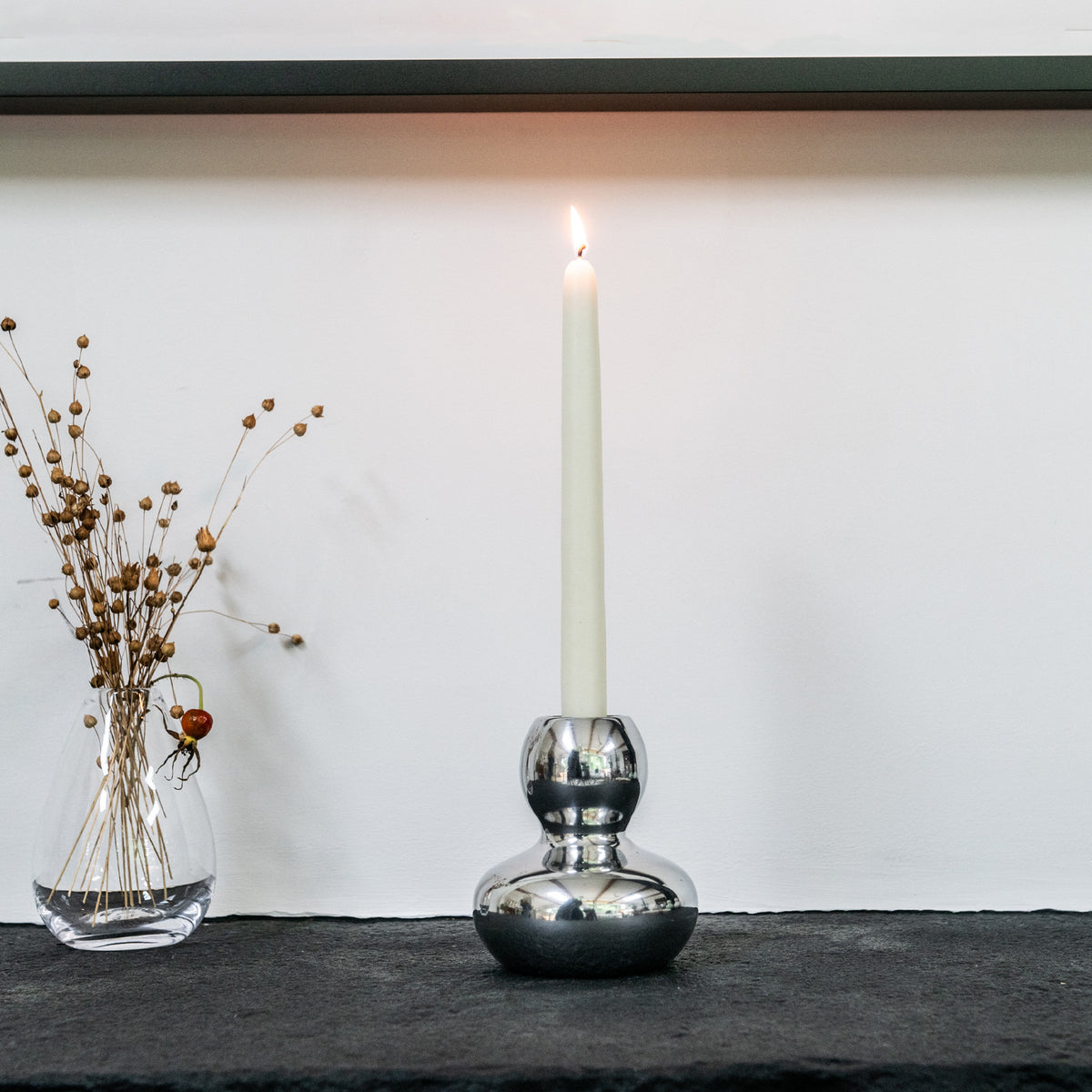 Silver aluminum candlestick with rounded bulbous base holding lit cream taper candle.