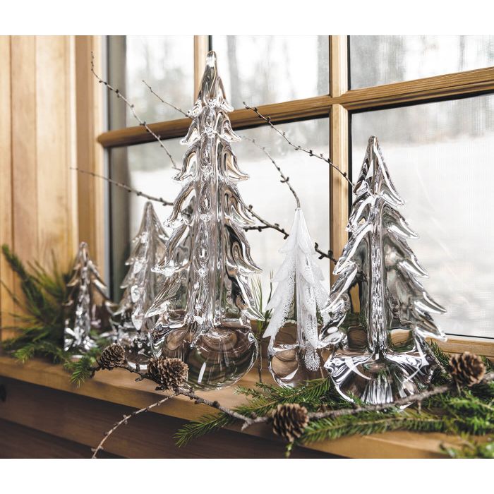 Clear glass tree-shaped decorations with frosted finish displayed on windowsill with evergreen branches and pinecones.