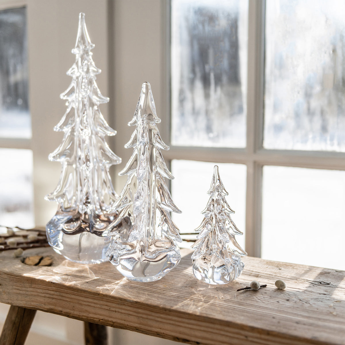 Three clear glass evergreen trees of graduated sizes displayed on a wooden surface.