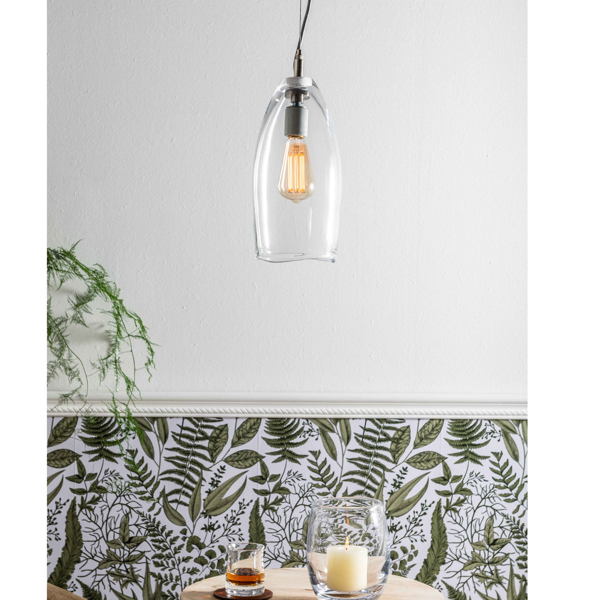 Clear glass pendant light with chrome fixture and warm-toned Edison-style bulb suspended from cord.