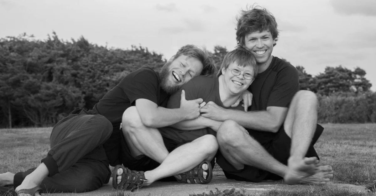 Three people laughing and embracing on a lawn in a black-and-white photo, capturing the joy and connection at the heart of LoveYourBrain
