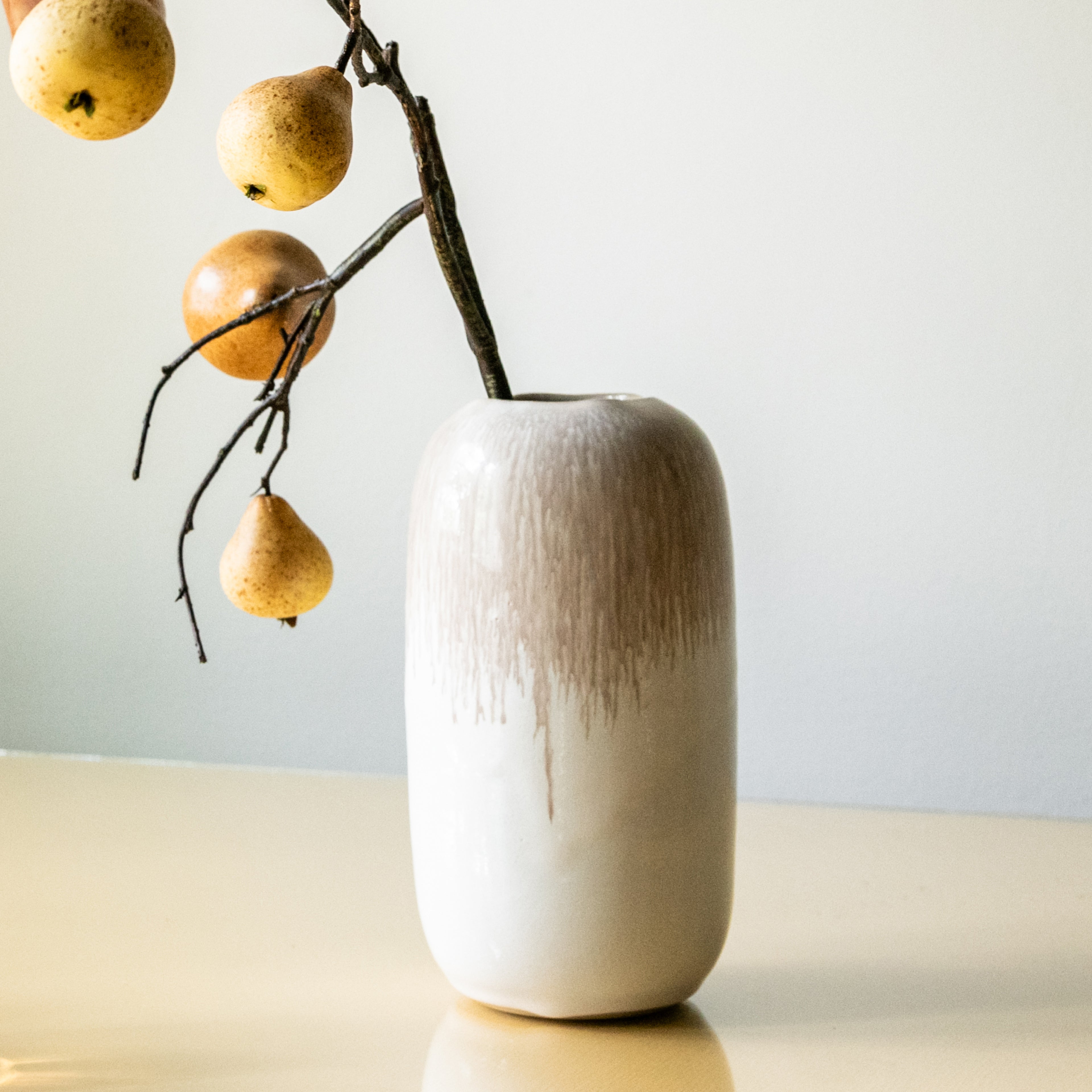 Cream-colored ceramic vase with textured surface holding a branch of decorative pears.