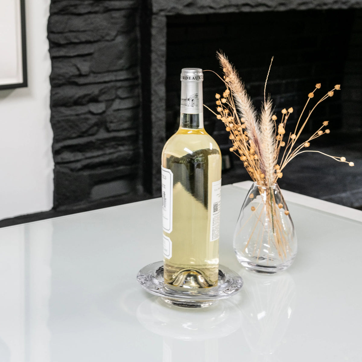 Clear glass coaster with decorative ridged border, holding white wine bottle on white surface.