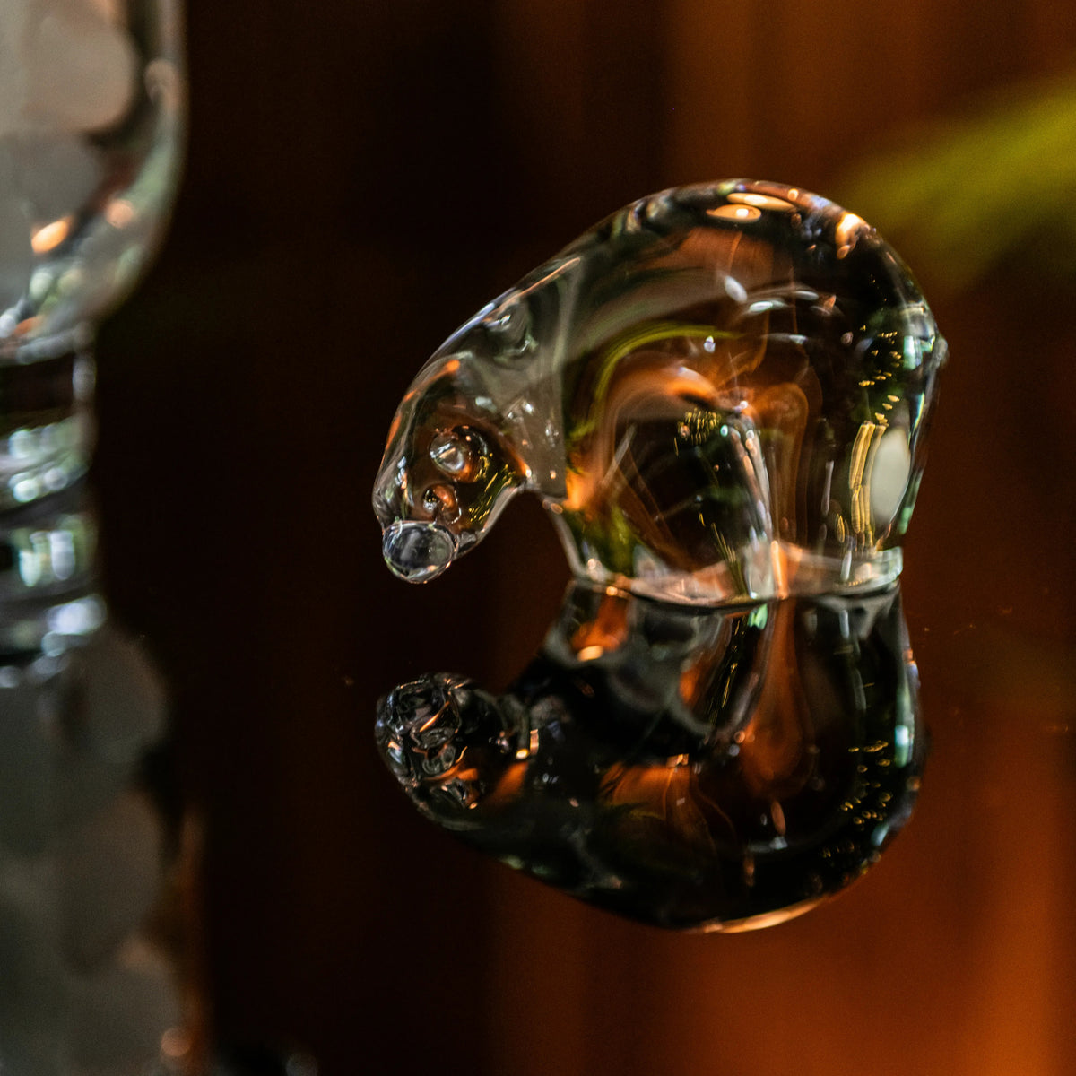 Small clear glass polar bear figurine with amber and dark tones, shown against a dark background.