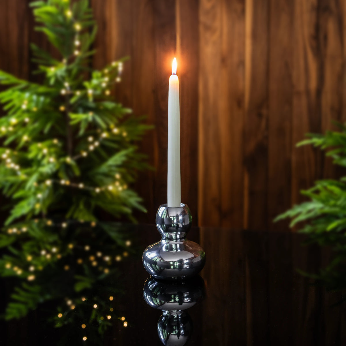 Polished aluminum candlestick with bulbous base holding a lit white taper candle against wooden background.