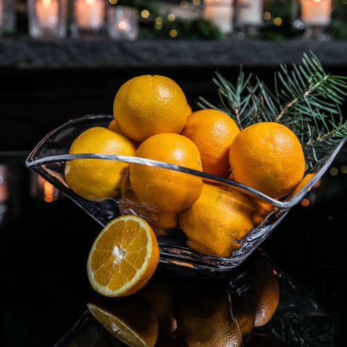 Black decorative bowl filled with fresh lemons and evergreen sprigs, one lemon halved.