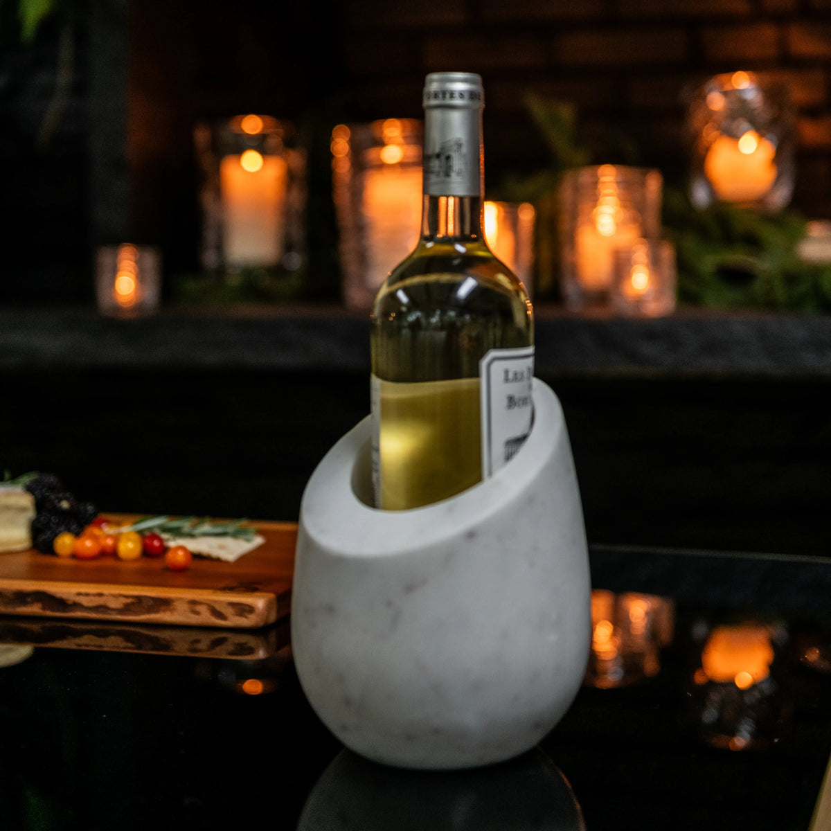 White marble wine chiller holding a wine bottle, displayed on a dark surface with candles in background.