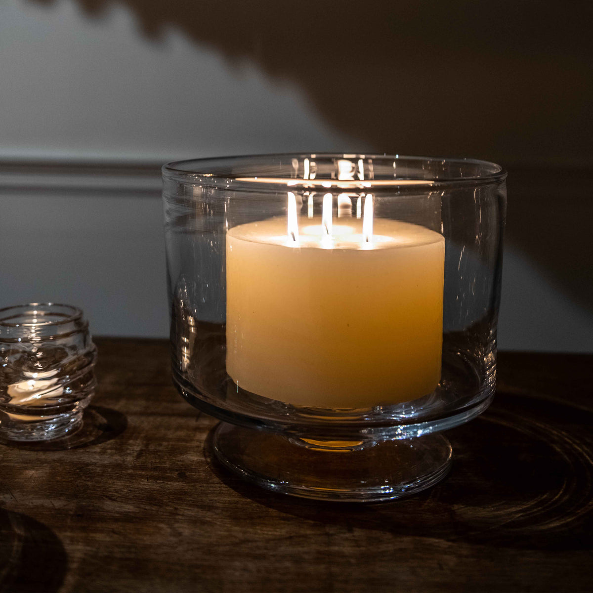Ivory pillar candle with three lit wicks inside a clear glass hurricane holder.