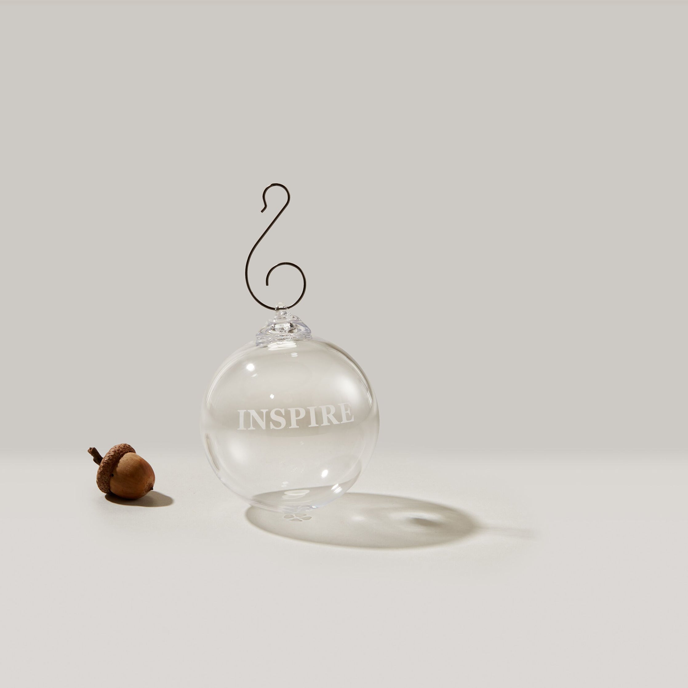 Clear glass round ornament with "INSPIRE" engraved text and metal hook, displayed with gift box.