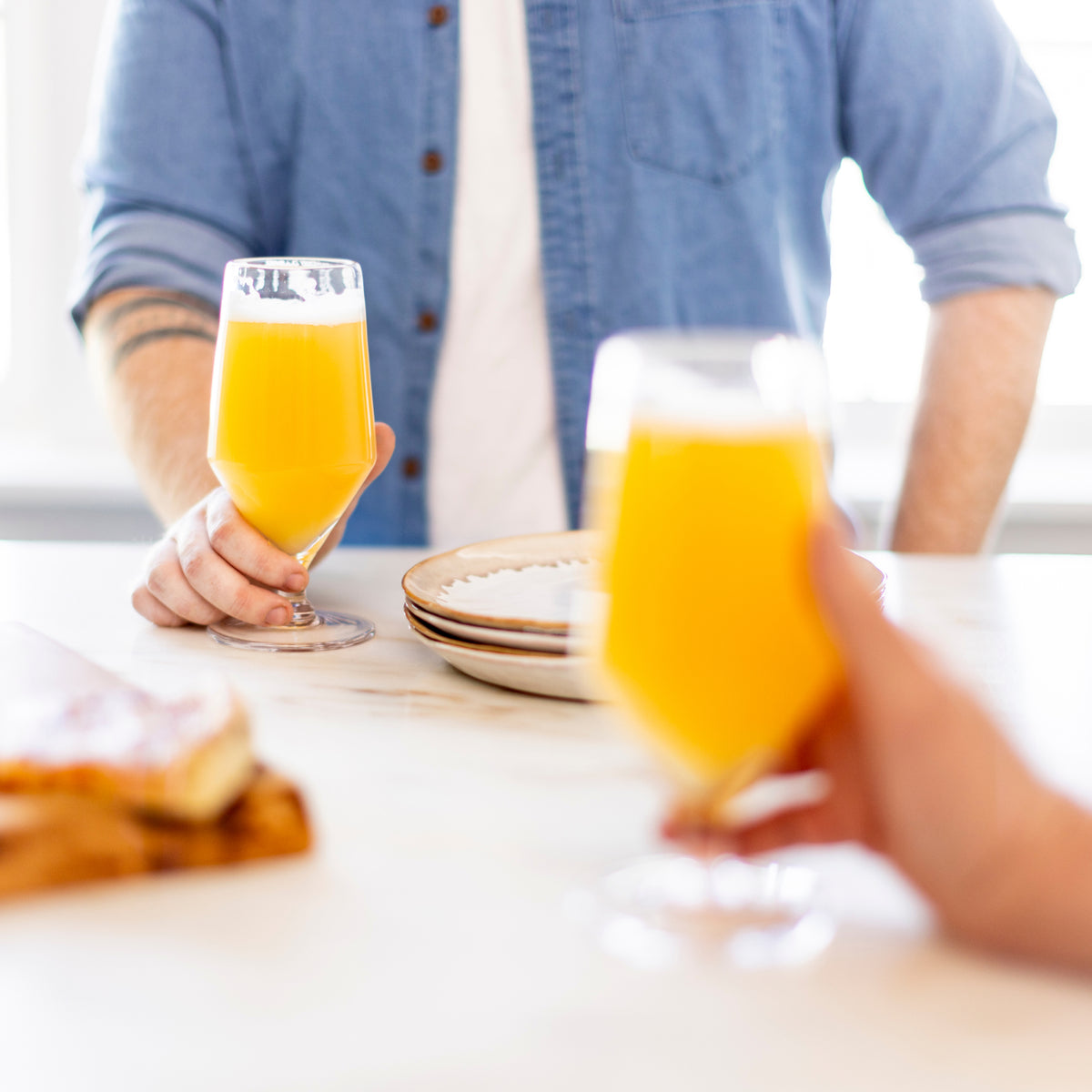 Two clear beer glasses filled with yellow beer, held by people at a table.