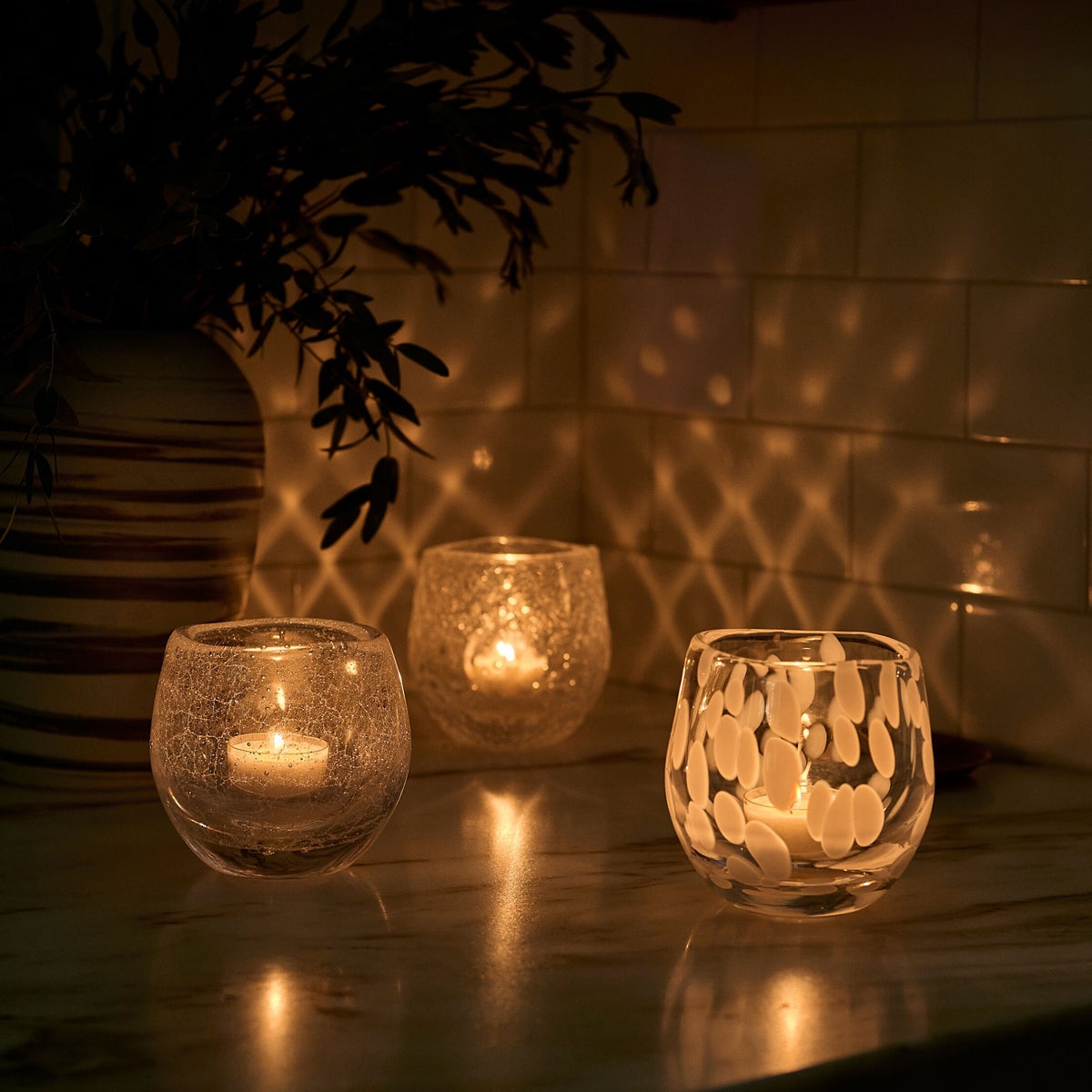 Three lit tealight candles in textured glass holders casting warm light and shadows.