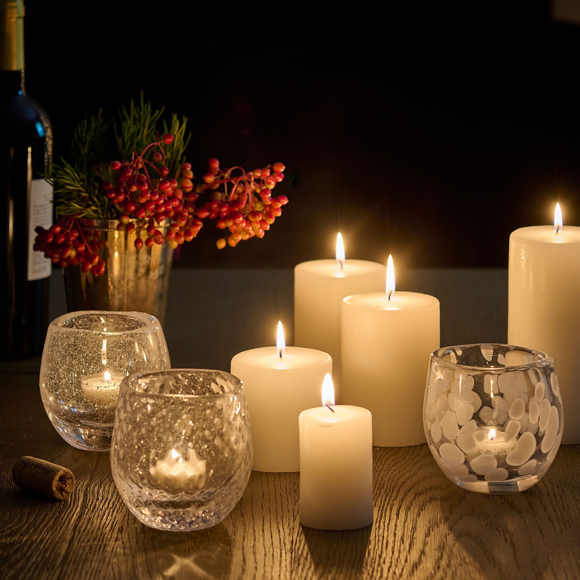 Clear glass tealight holders with textured patterns containing lit candles, arranged with cream pillar candles on a wooden su