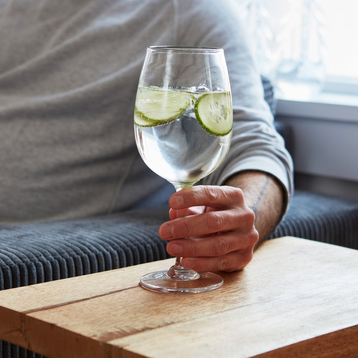 Person holding a clear wine glass with clear liquid and lime slices on a wooden table.